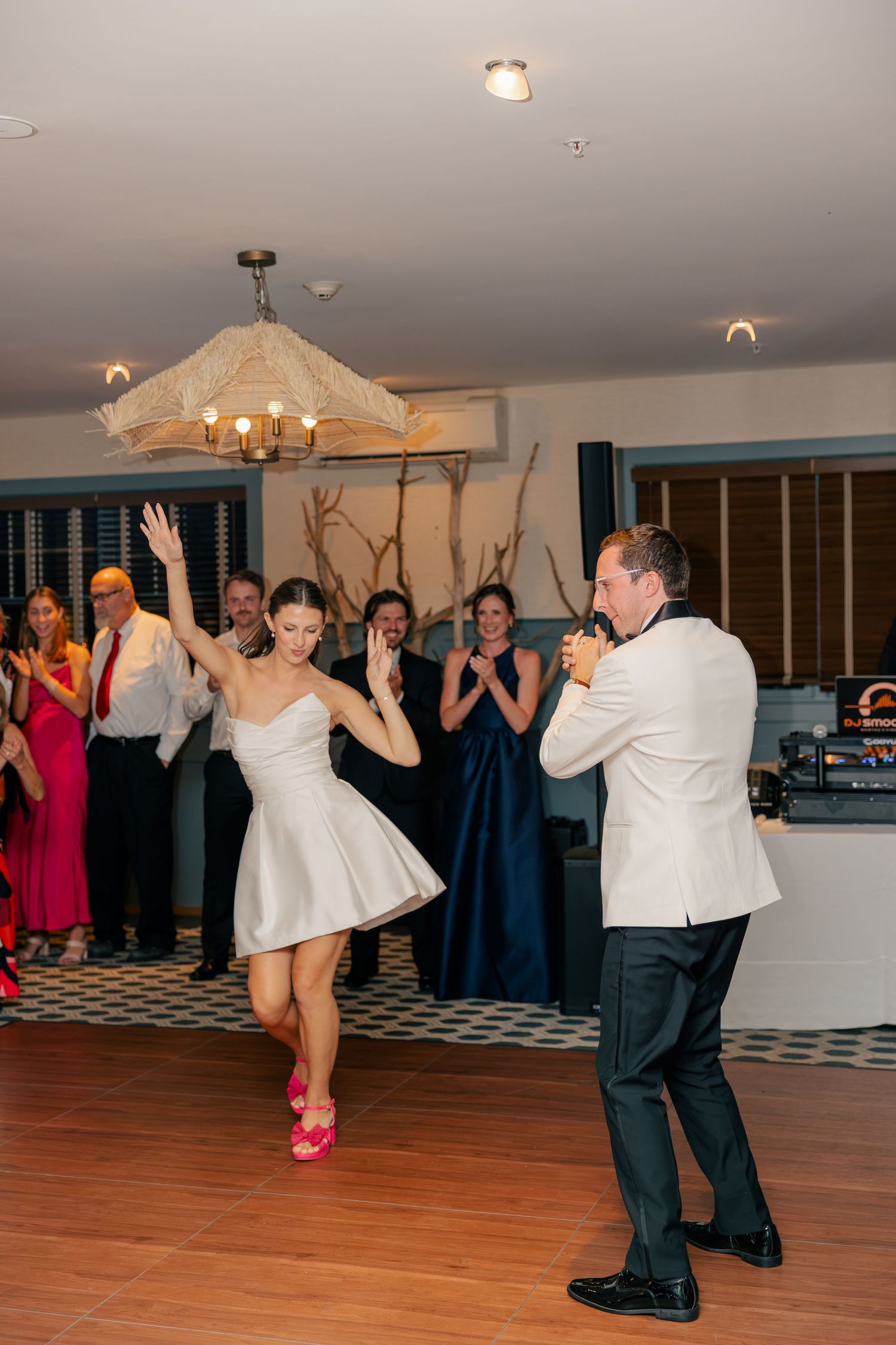 Bride and groom share a lively first dance at their wedding reception while guests cheer and applaud in the background.