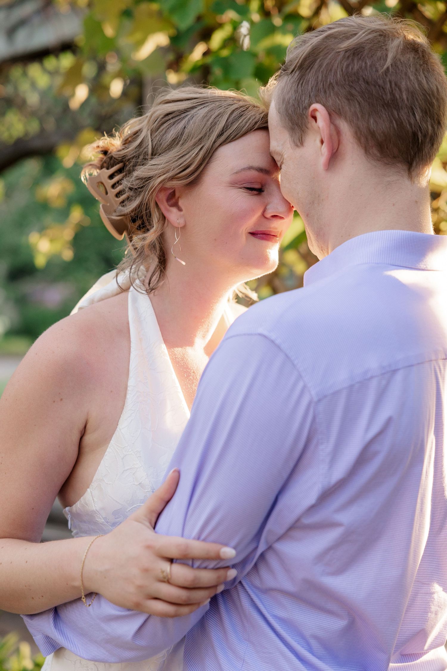 Romantic couple embraces in a sunlit garden setting with soft natural lighting and greenery in the background.
