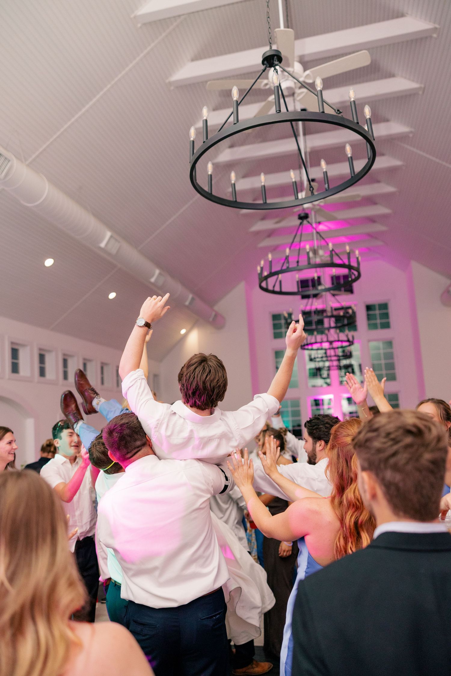 Energetic wedding reception dance floor with guests celebrating under a chandelier.