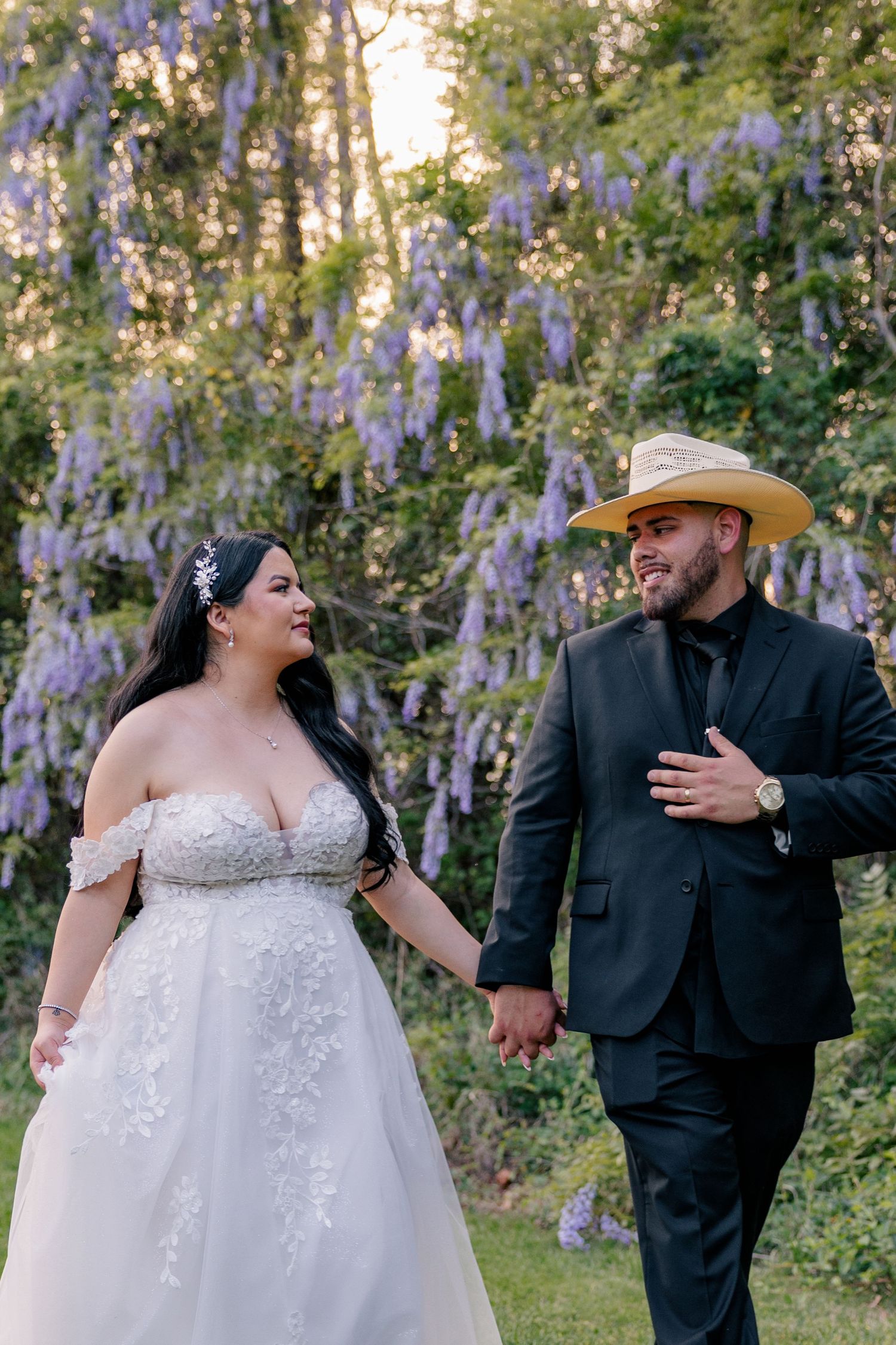 Candid wedding couple sharing joyful laughter among blooming wisteria flowers.