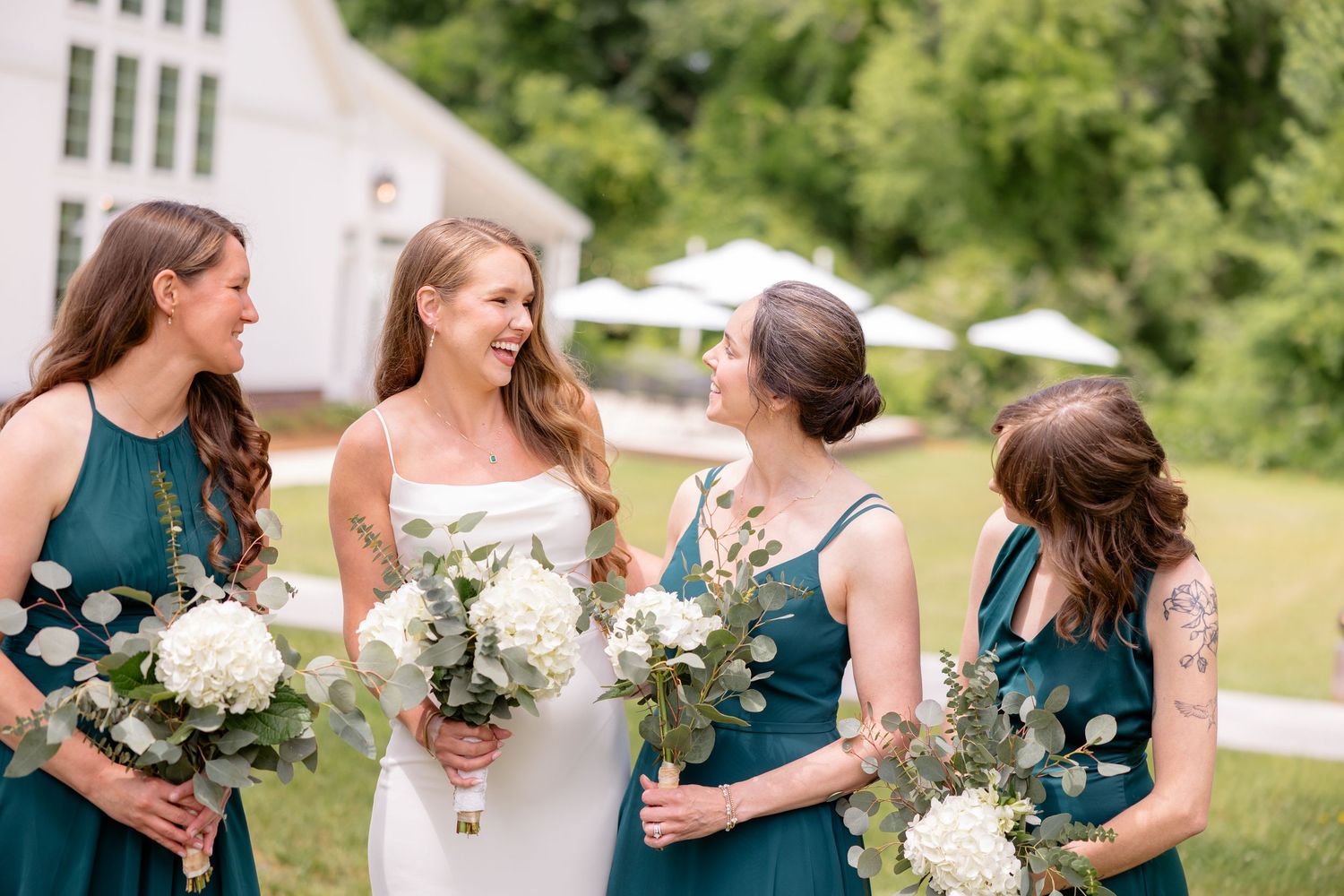 Bridesmaids in teal dresses holding white bouquets during an outdoor wedding ceremony.