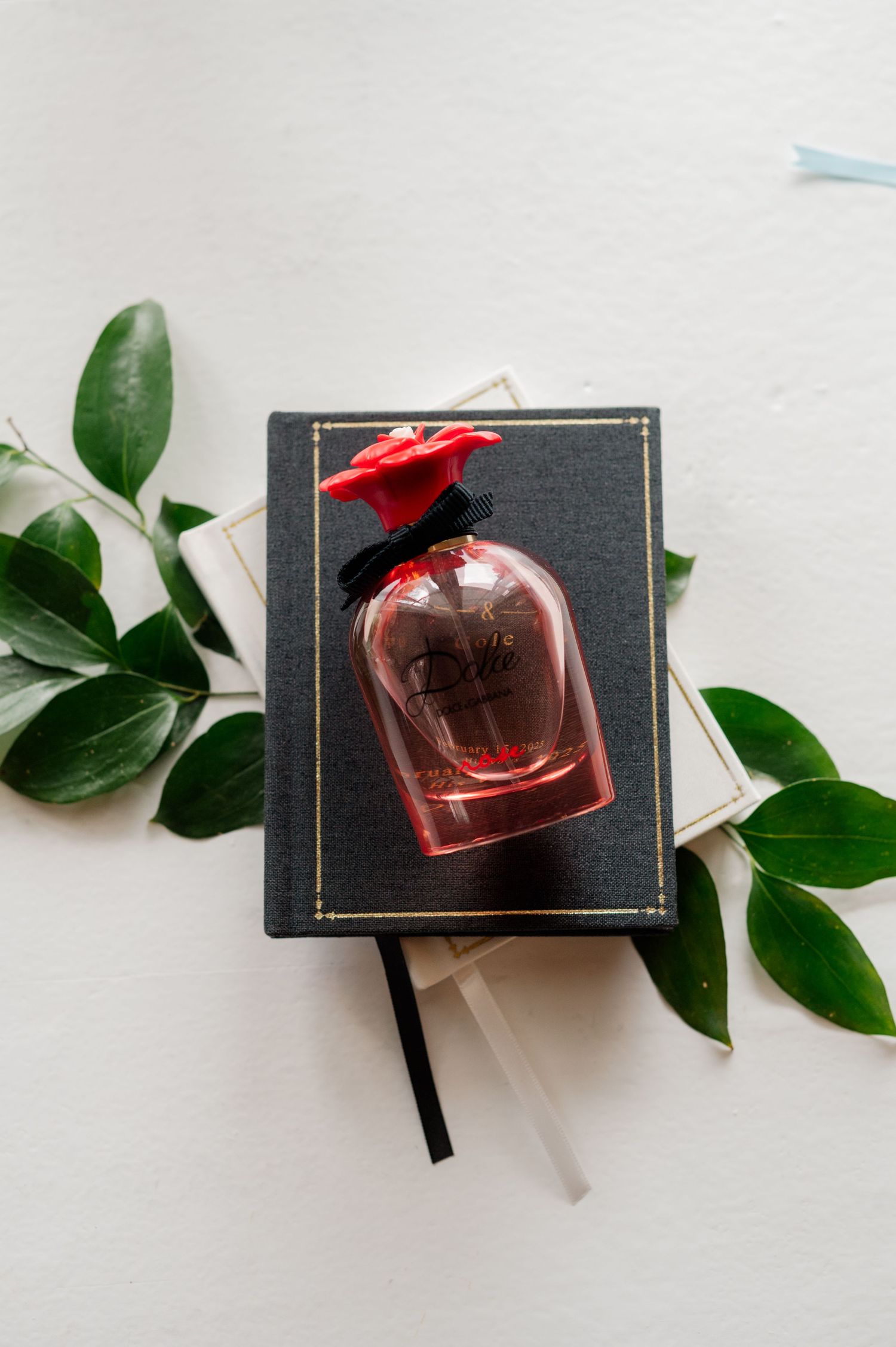 Pink perfume bottle displayed on black book with green leaves for decoration.