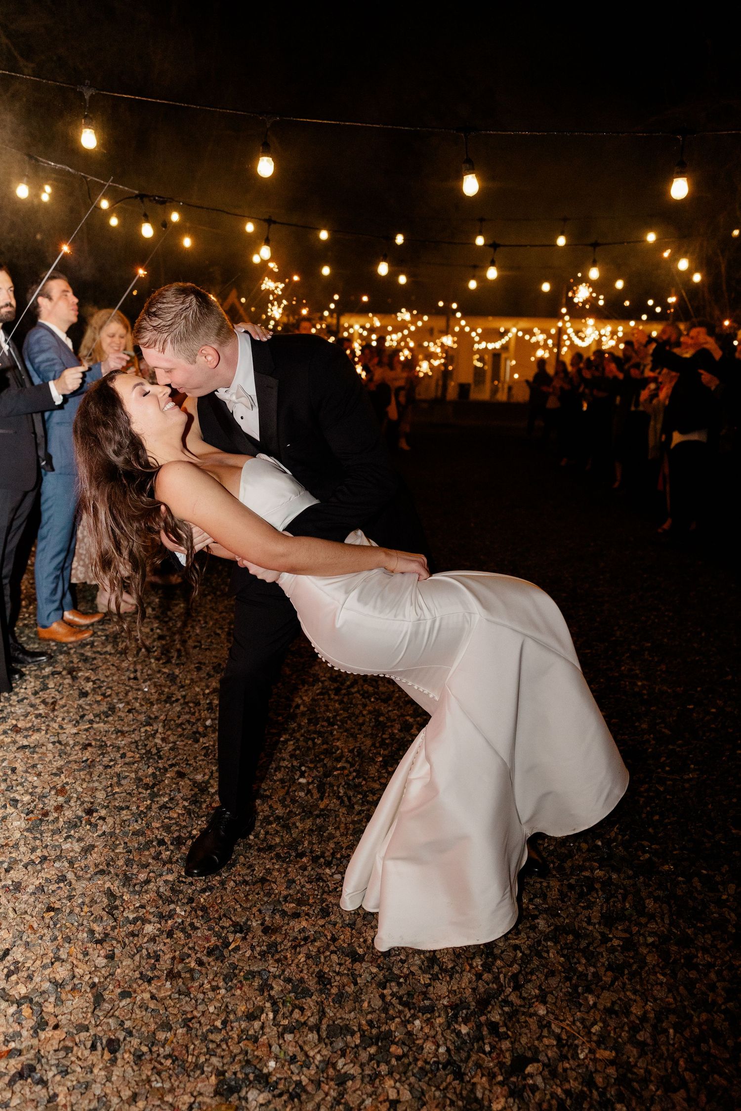 Romantic dance dip under string lights at outdoor nighttime wedding reception.