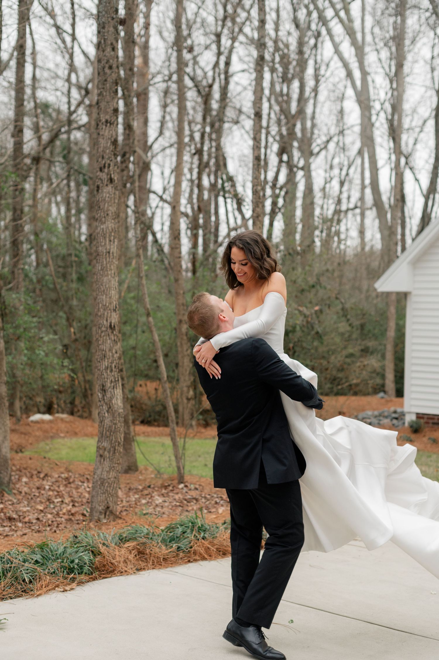 A couple taking romantic outdoor photos in a wooded area with the bride's dress flowing in the wind.