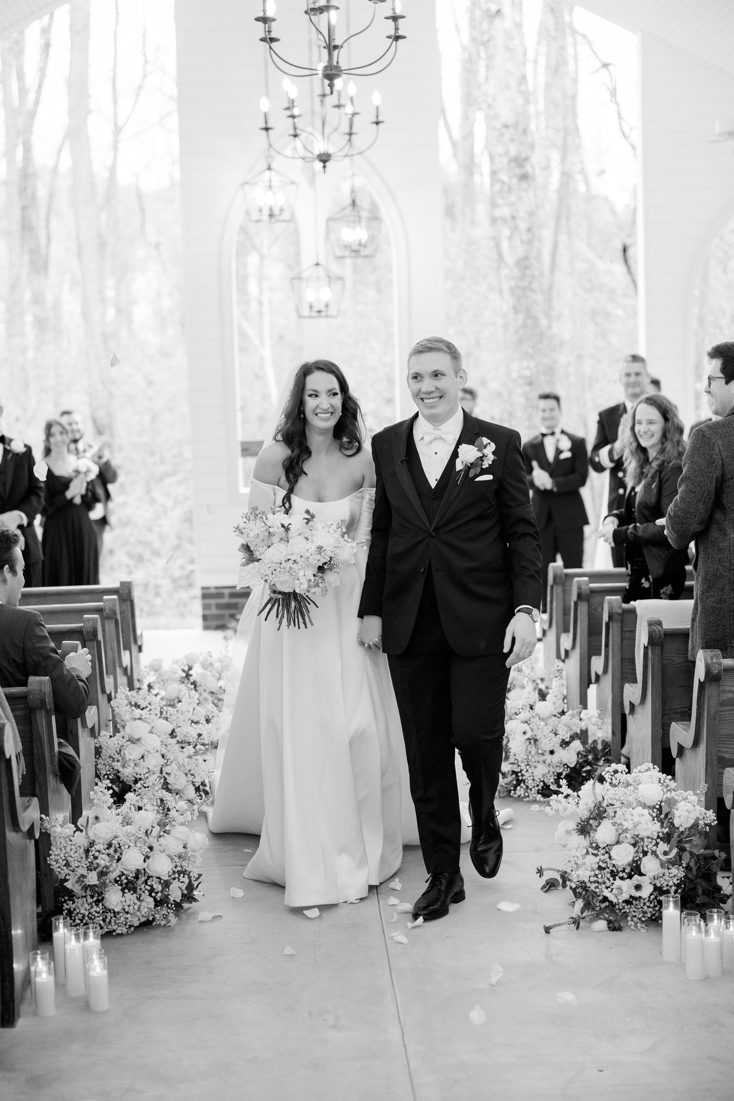 Wedding ceremony exit in church aisle decorated with white flowers and candles.