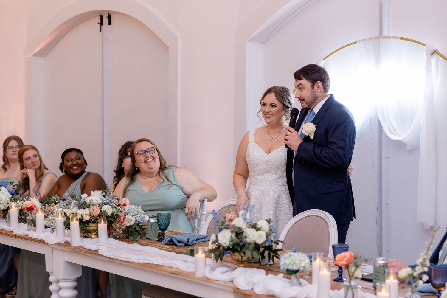 Wedding guests enjoying speeches and celebrations in an elegant white venue.