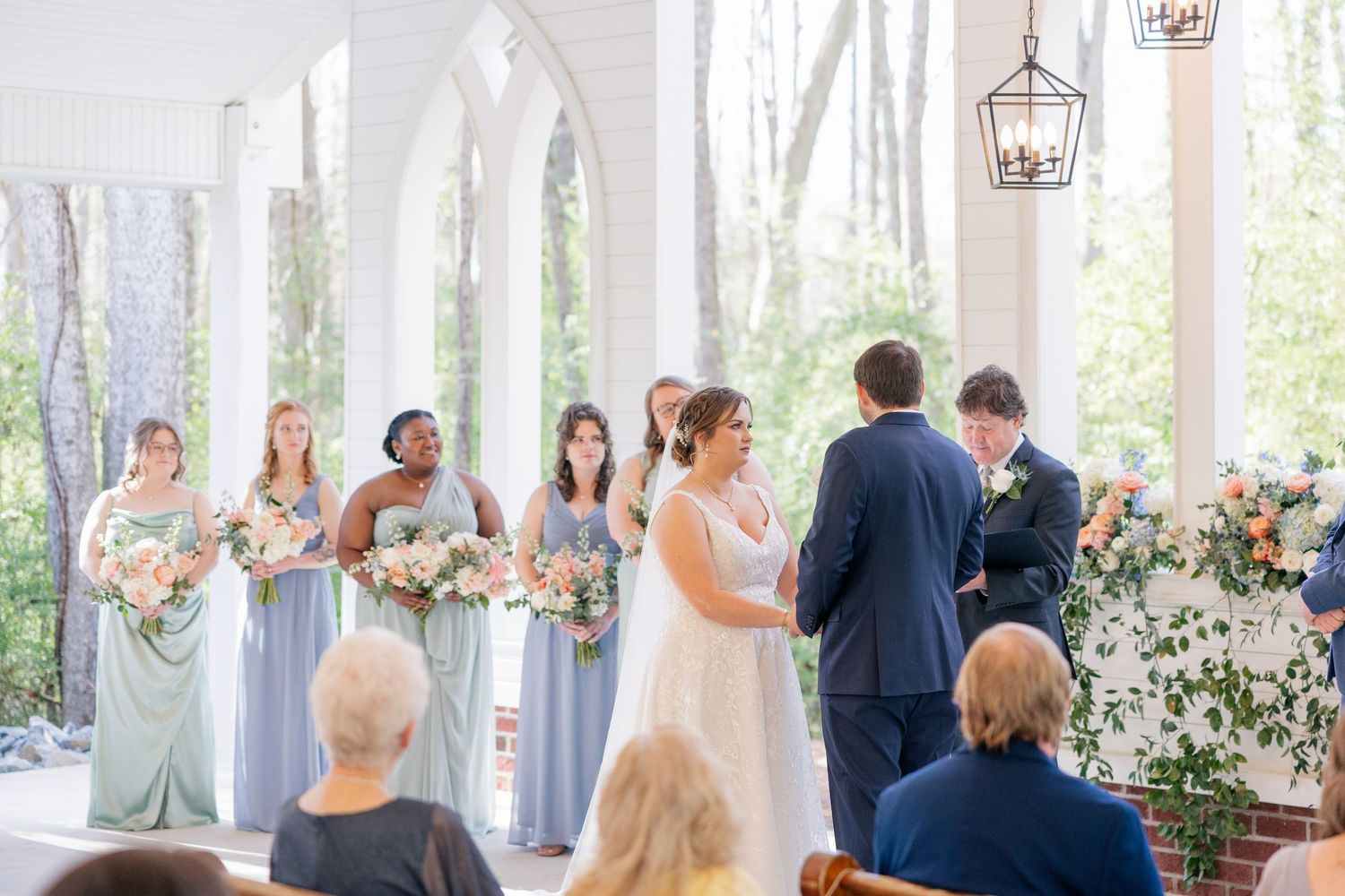 Light-filled wedding ceremony space with white draping and floral arrangements at the altar.