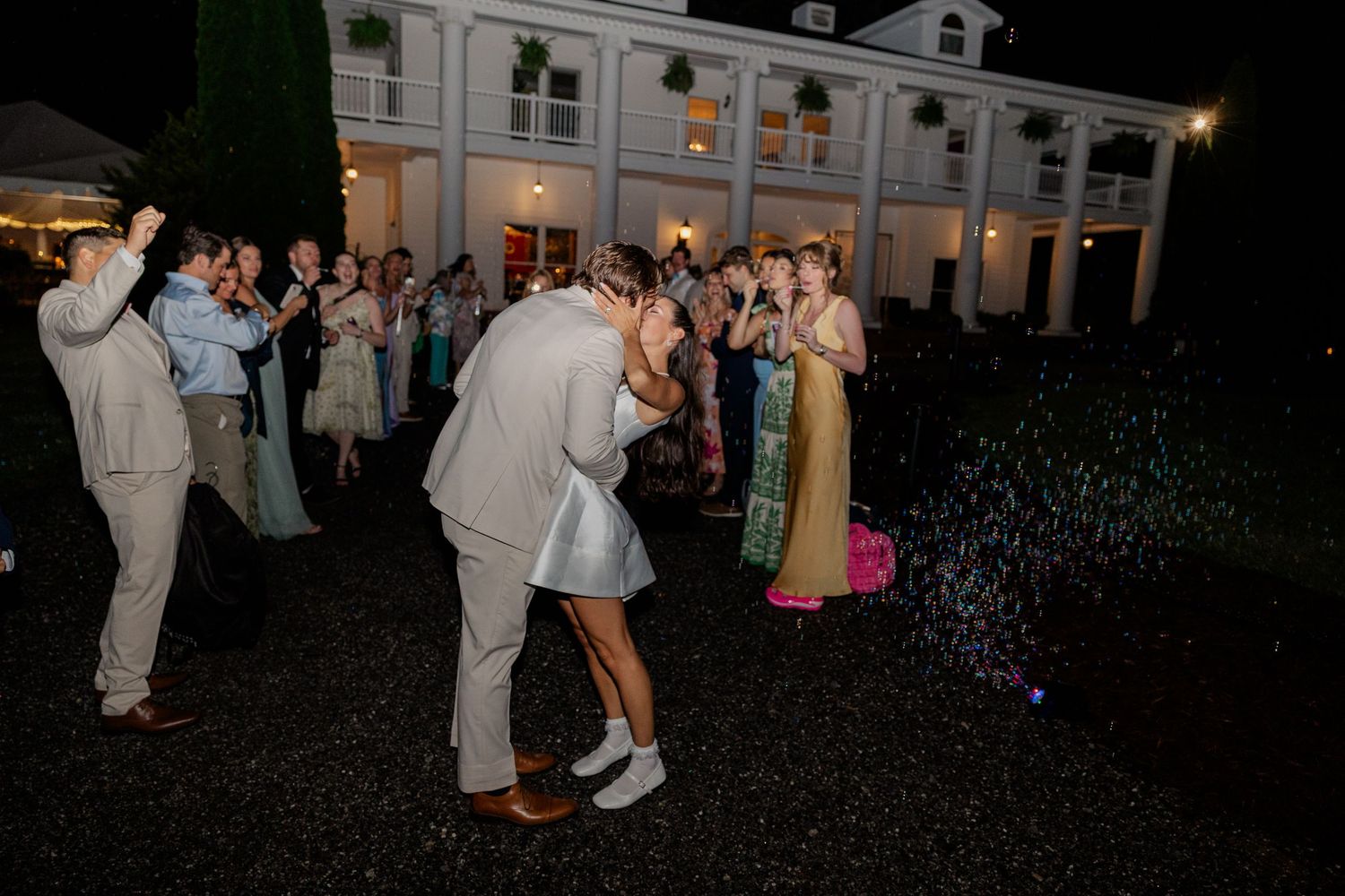 Wedding reception dance party at night with guests celebrating outside a grand white building.