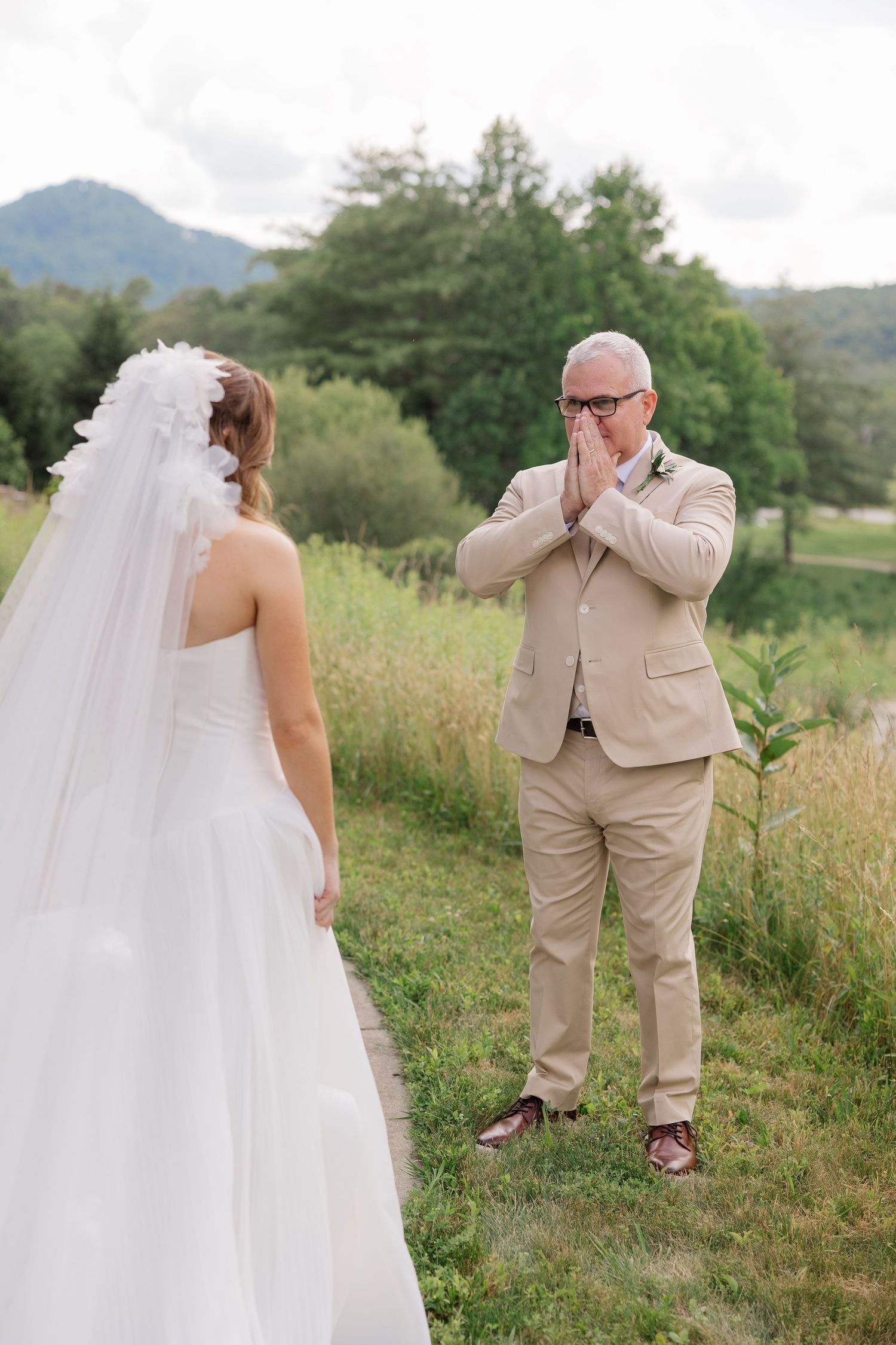 Emotional first look moment in a grassy field with mountains in the background.