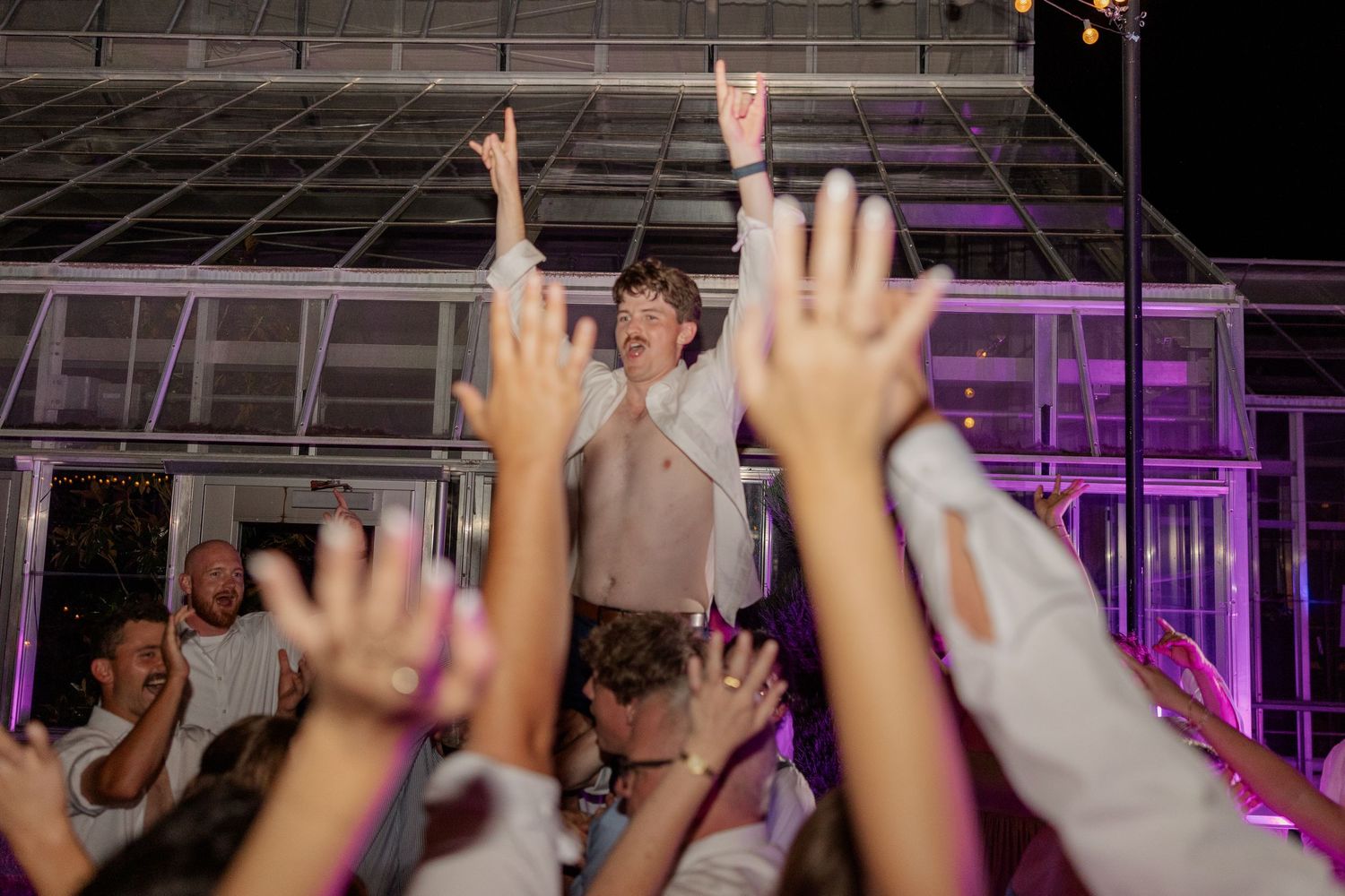 Silhouetted crowd with raised hands dancing under purple event lighting.