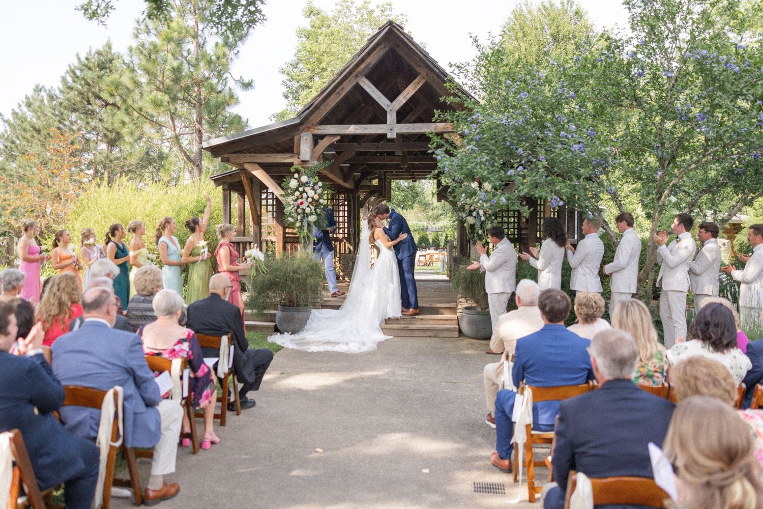 Wedding ceremony takes place in a rustic outdoor venue with wooden pavilions and natural surroundings.