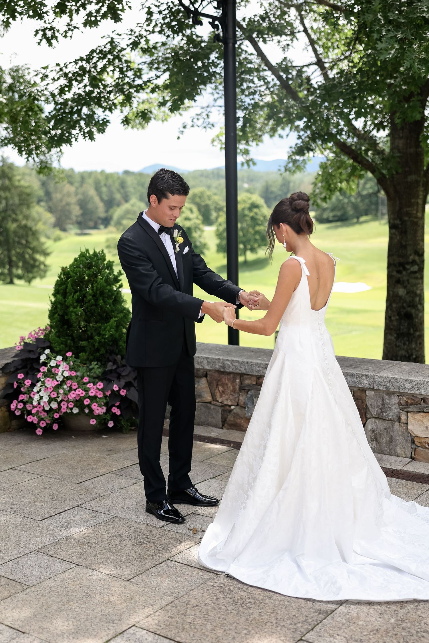 Bride and groom share a first look moment on a stone patio, with lush green golf course views in the background.