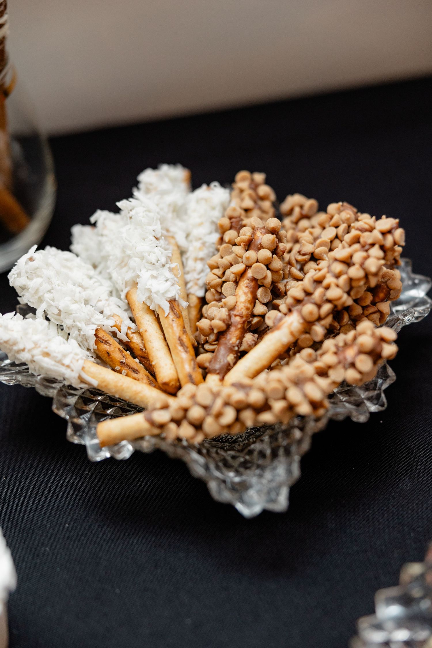 Decorative platter of white coconut and brown chocolate covered pretzel sticks arranged in a crystal dish.