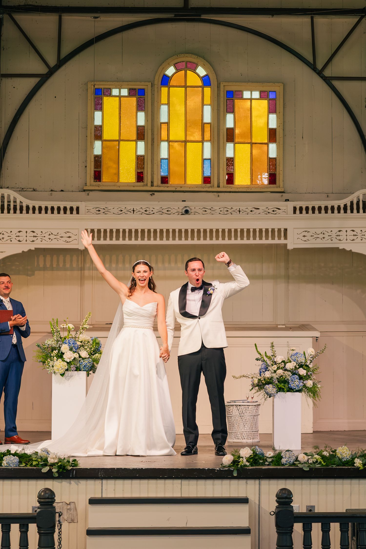 Joyful bride and groom celebrate at wedding altar with stained glass windows and floral arrangements.
