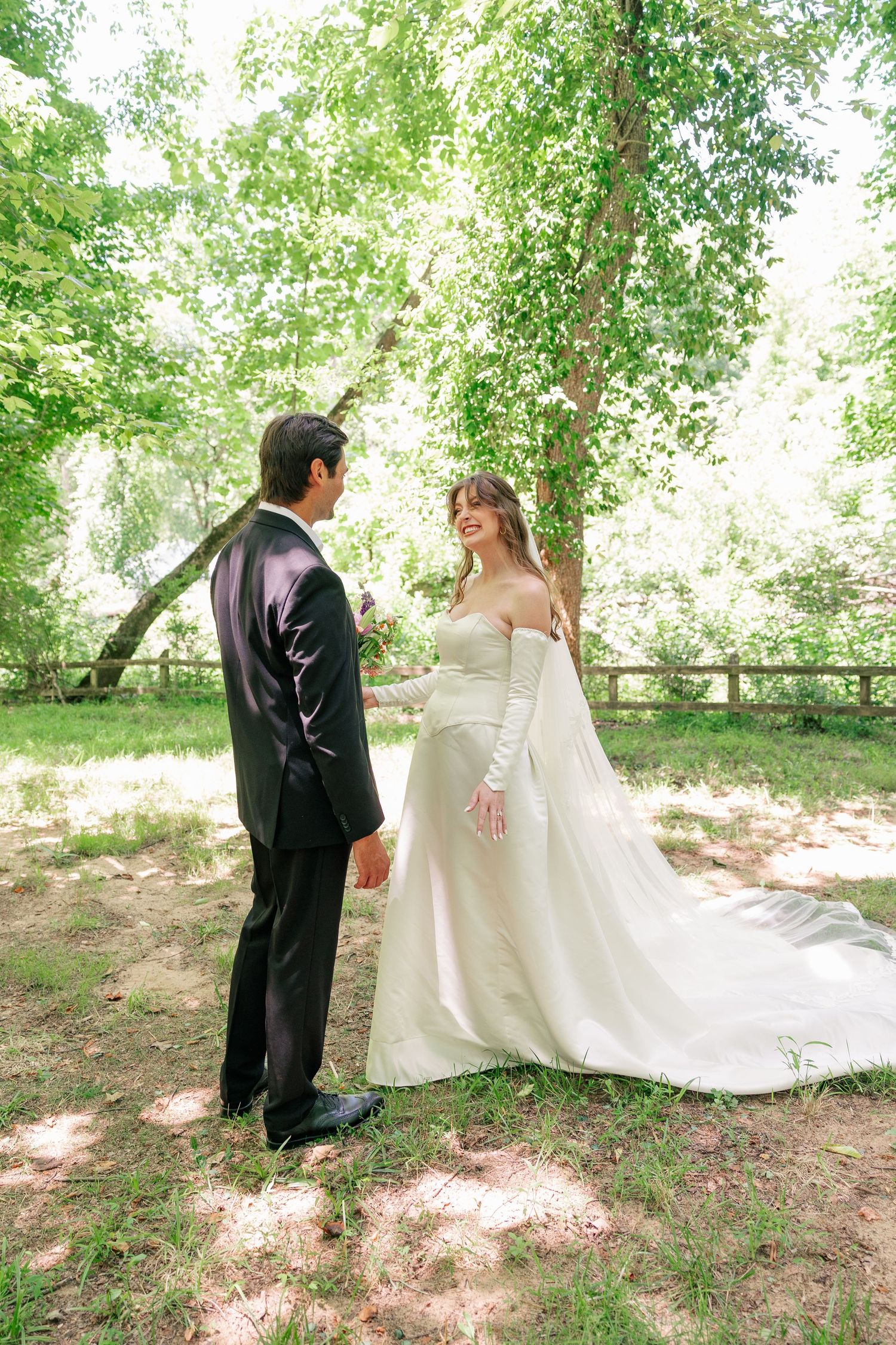 Bride and groom share a romantic moment among lush green trees in an outdoor wedding setting.