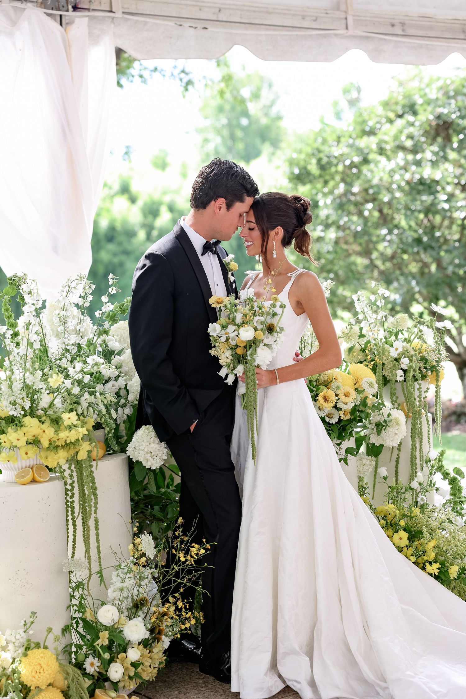 Romantic wedding couple shares intimate moments under white tent with lush floral arrangements and natural lighting. Biltmore Forrest Club