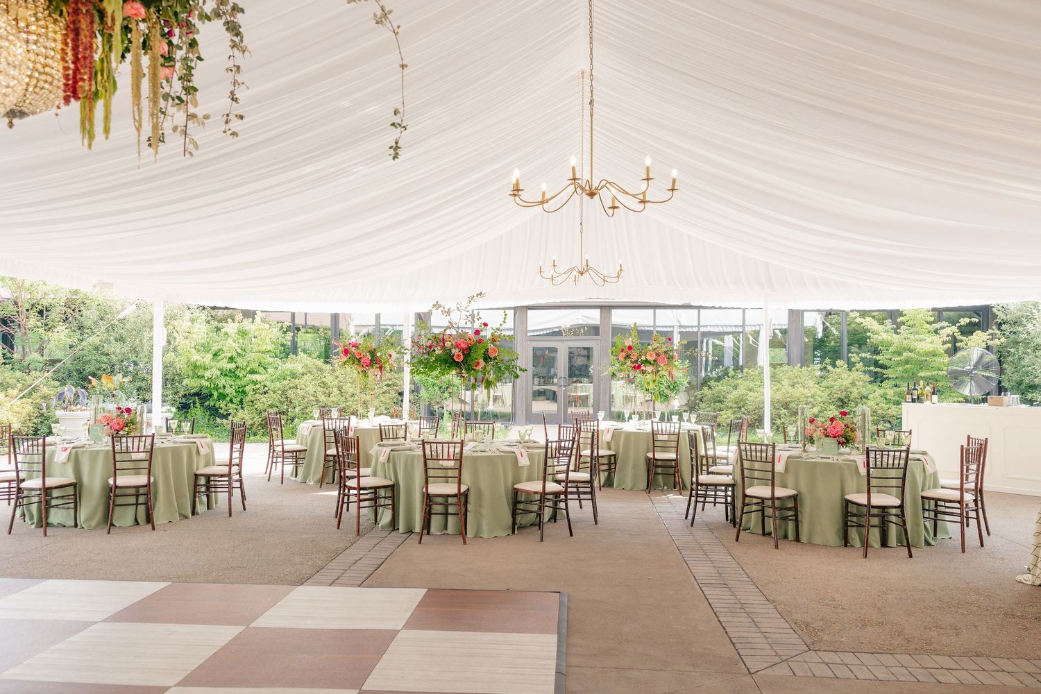Spacious wedding reception tent with sage green linens, chiavari chairs, and pink floral centerpieces.