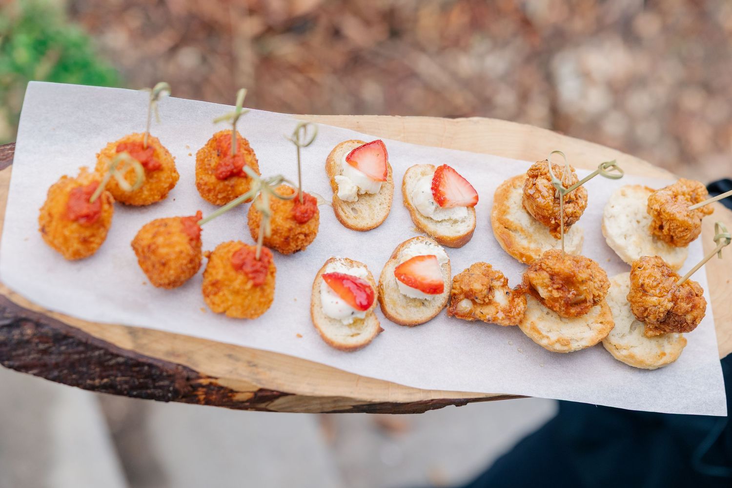 Elegant wedding appetizer display featuring fried bites, strawberry crostini, and crispy hors d\u2019oeuvres on a wood board.