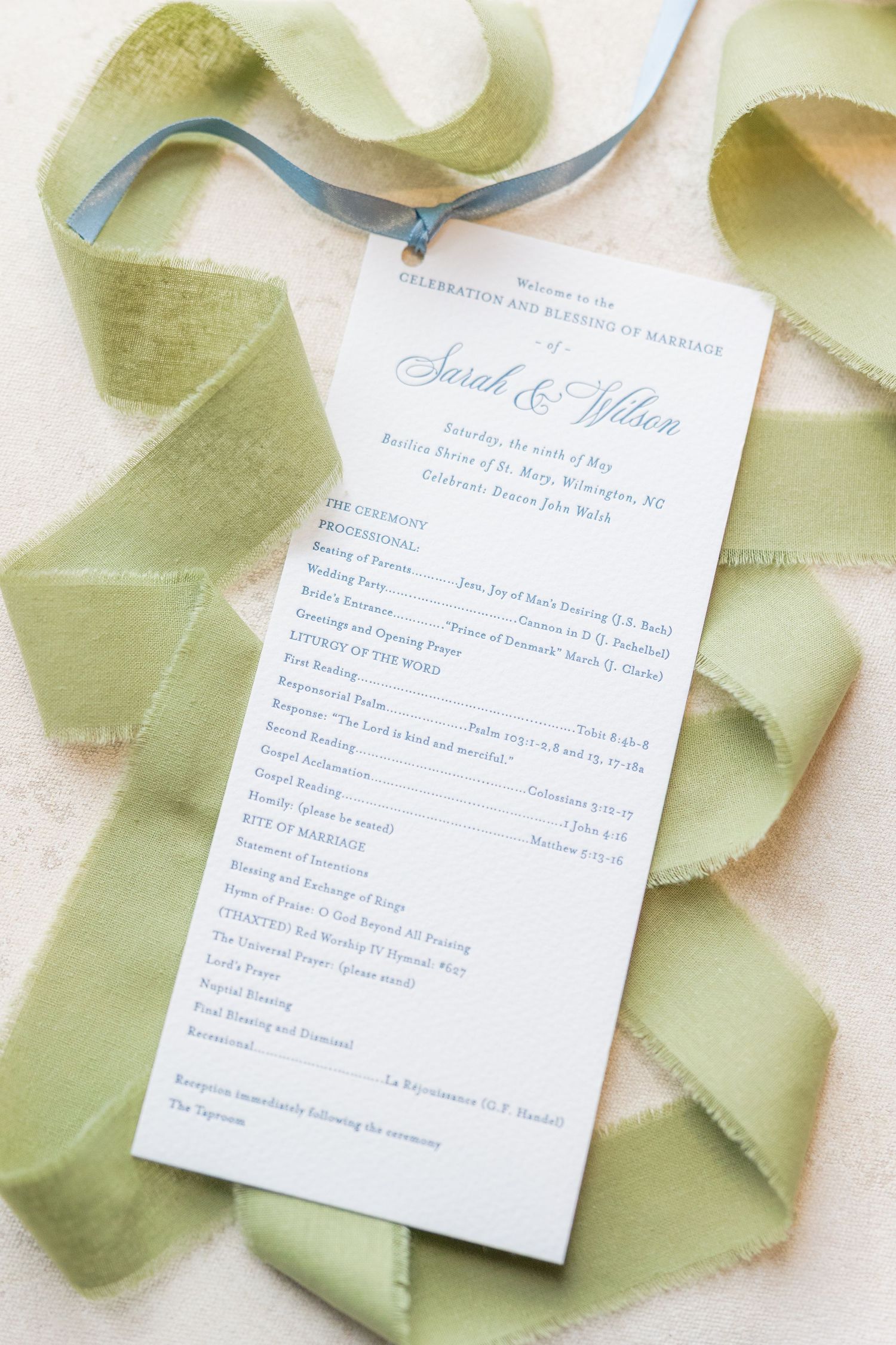 Elegant wedding ceremony program for Sarah and Wilson displayed with sage green and blue silk ribbons.
