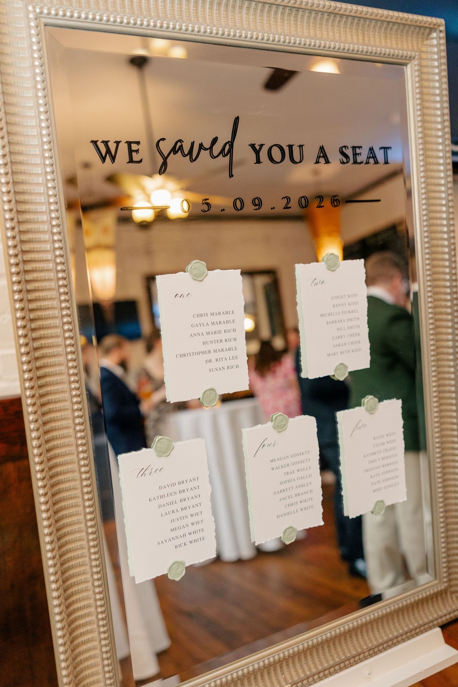 Elegant mirrored seating chart display reading We Saved You A Seat with date 05.09.2025 at wedding reception.