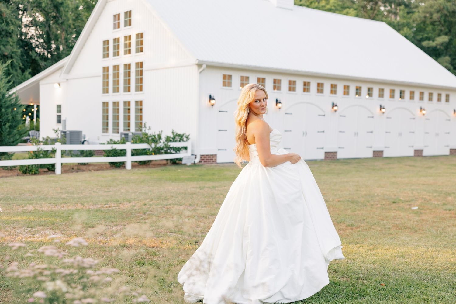 Bride in white ball gown twirling in front of a white barn wedding venue outdoors.