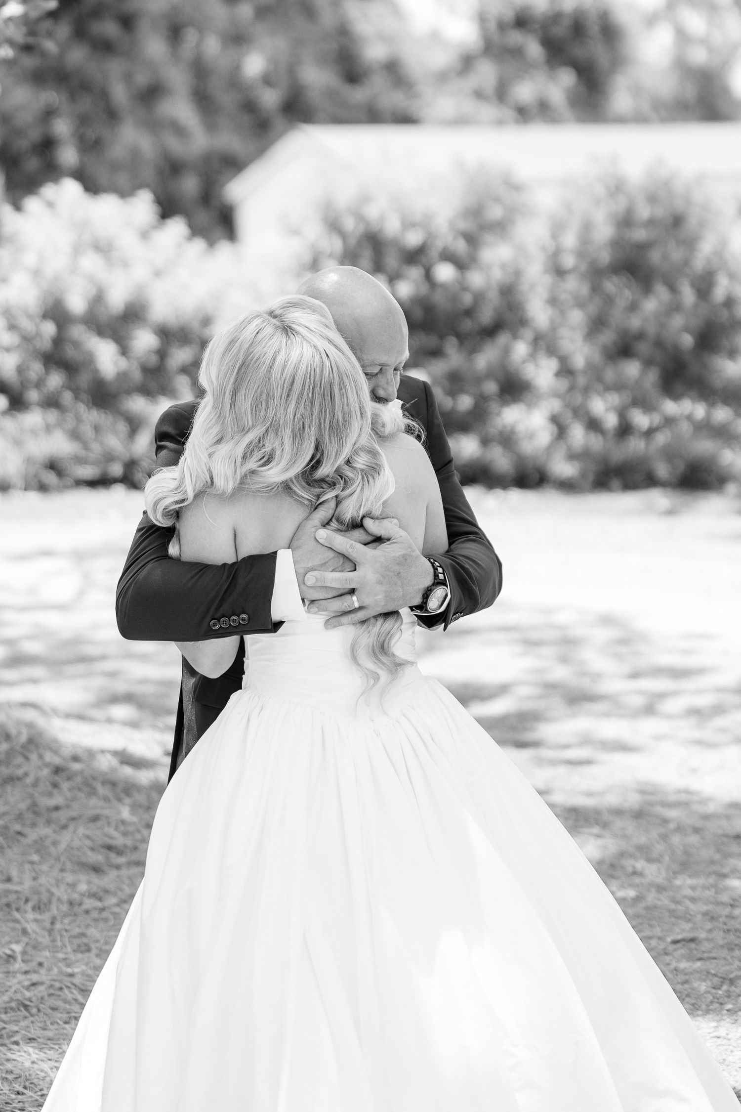Black and white photo of groom embracing bride in strapless ball gown outdoors after wedding ceremony.