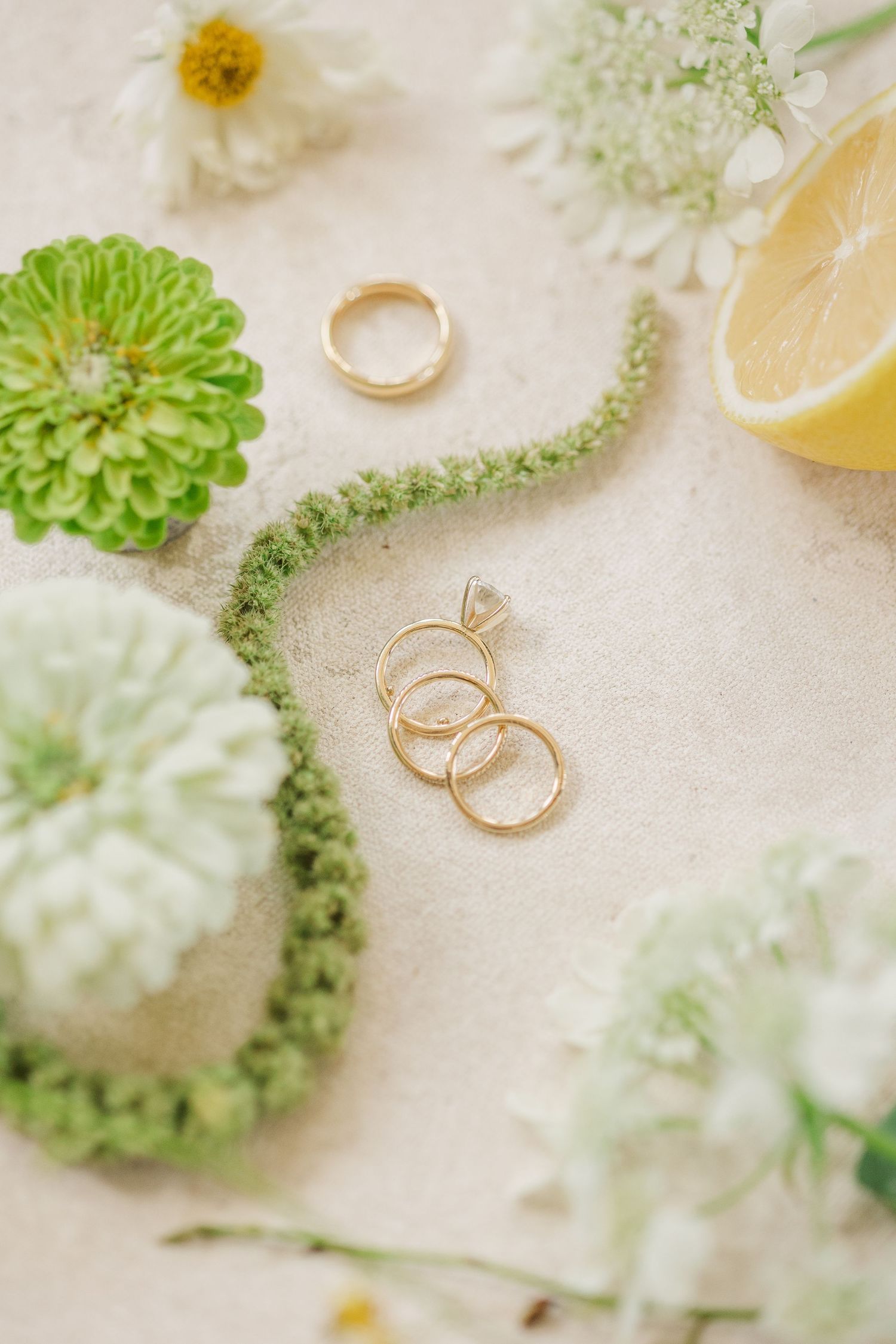 Wedding rings and delicate green floral decorations arranged on a light textured surface.