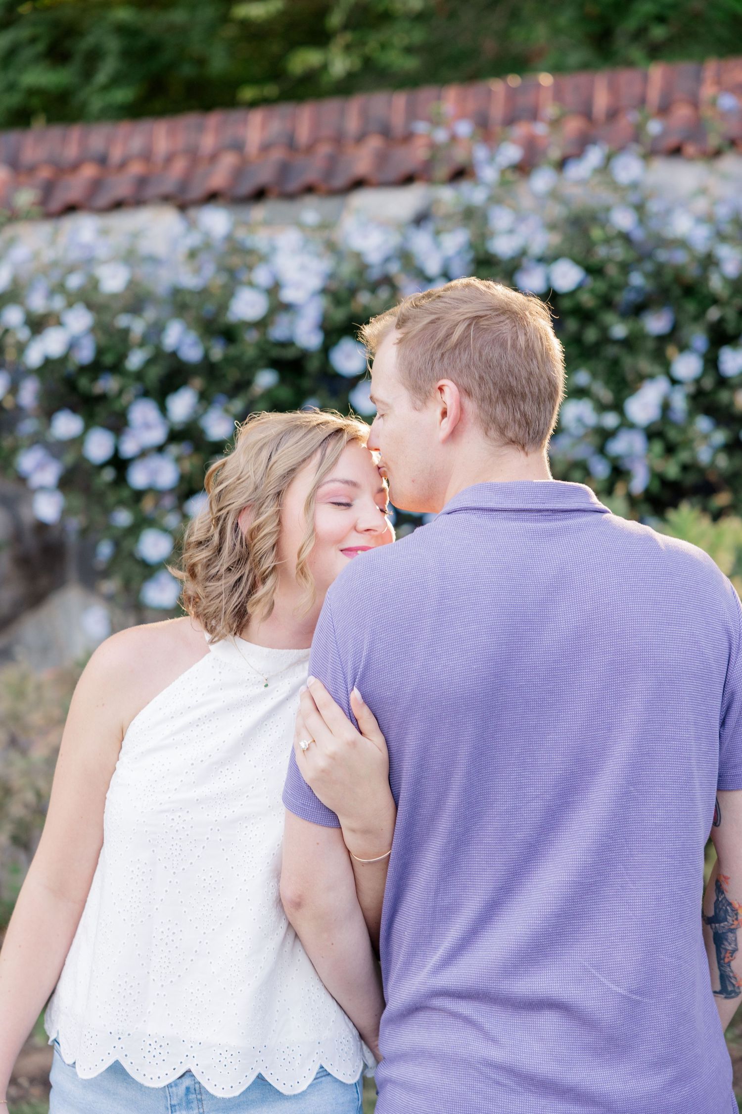 A romantic couple shares tender moments in a garden setting with blue flowers in the background.