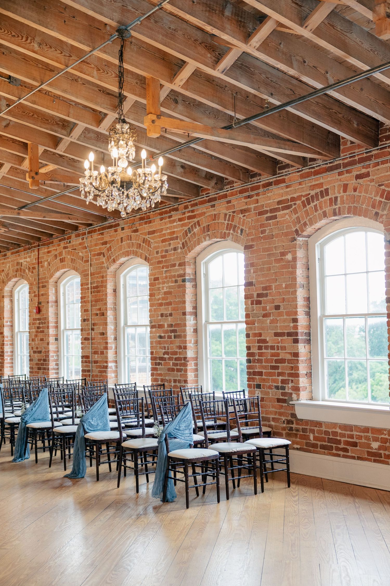 Elegant wedding ceremony setup in a rustic brick venue with chiavari chairs and blue sash ribbons.