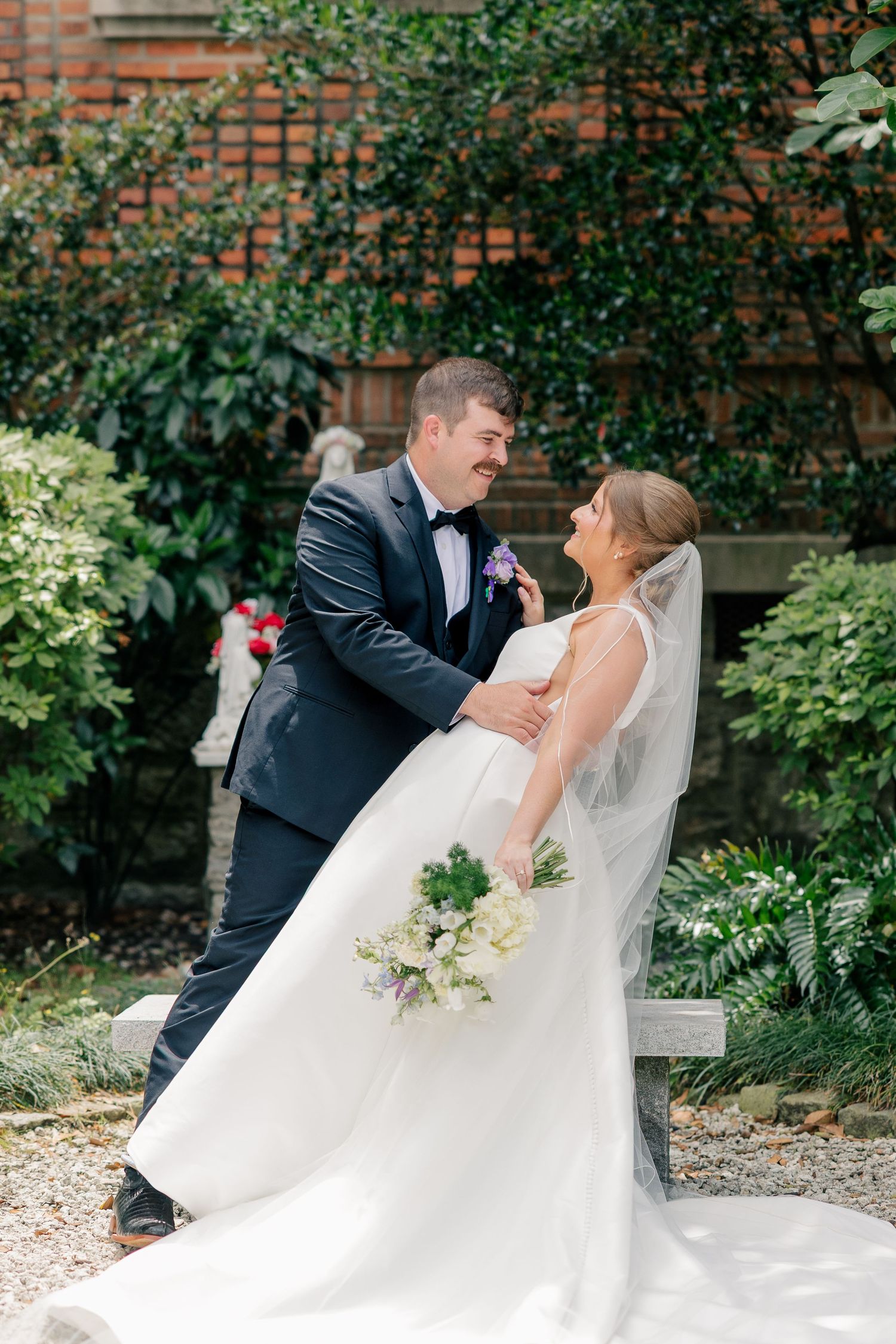 Bride and groom share a romantic moment in a lush garden, her veil flowing gracefully.
