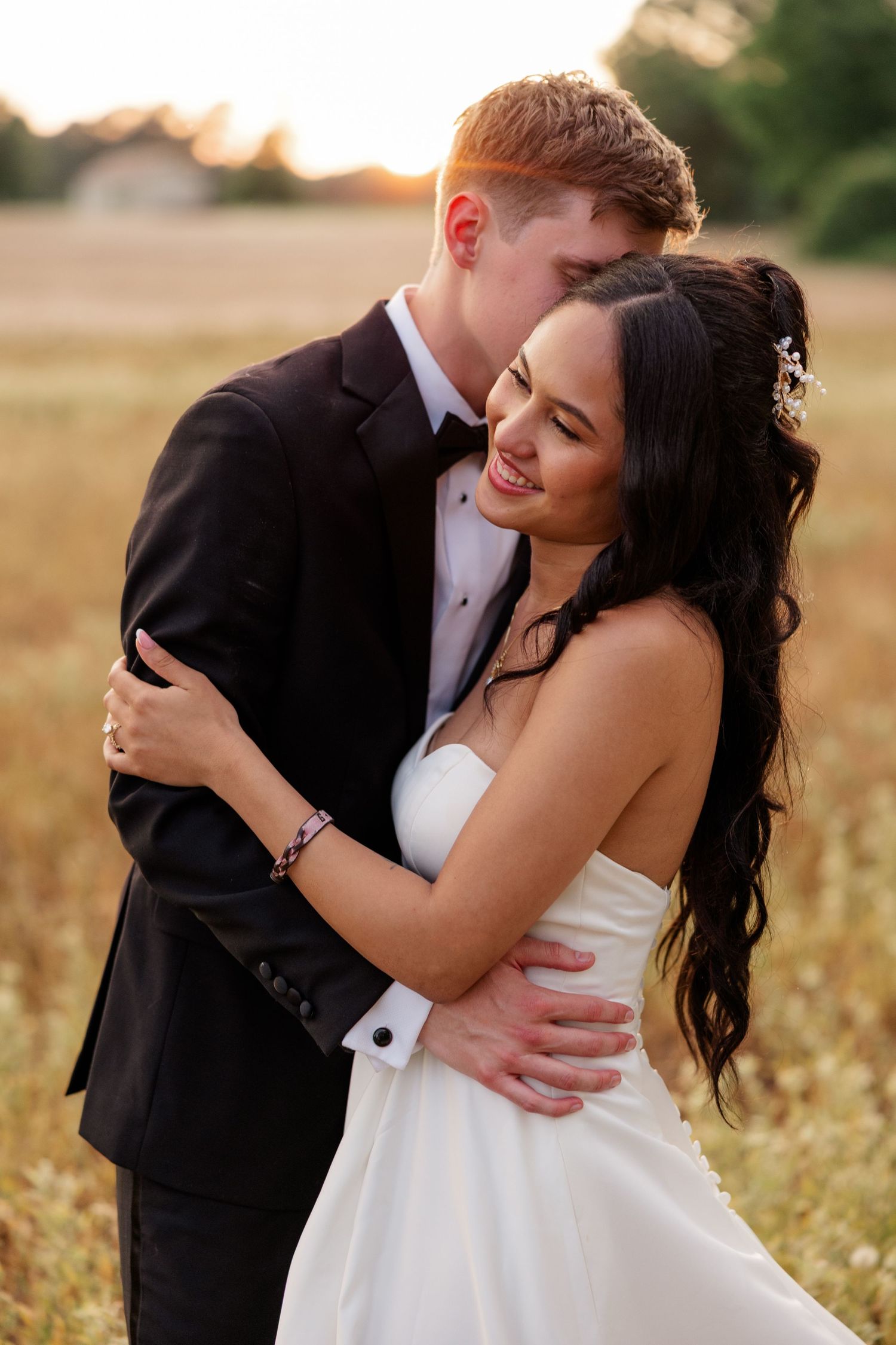 A romantic couple embraces in a sunlit field during golden hour wearing formal wedding attire.