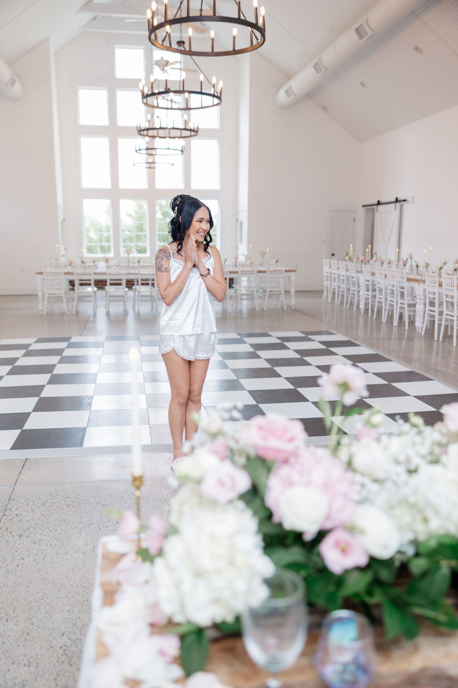 Bright reception hall with checkered floor, chandeliers and floral arrangements on wooden tables.