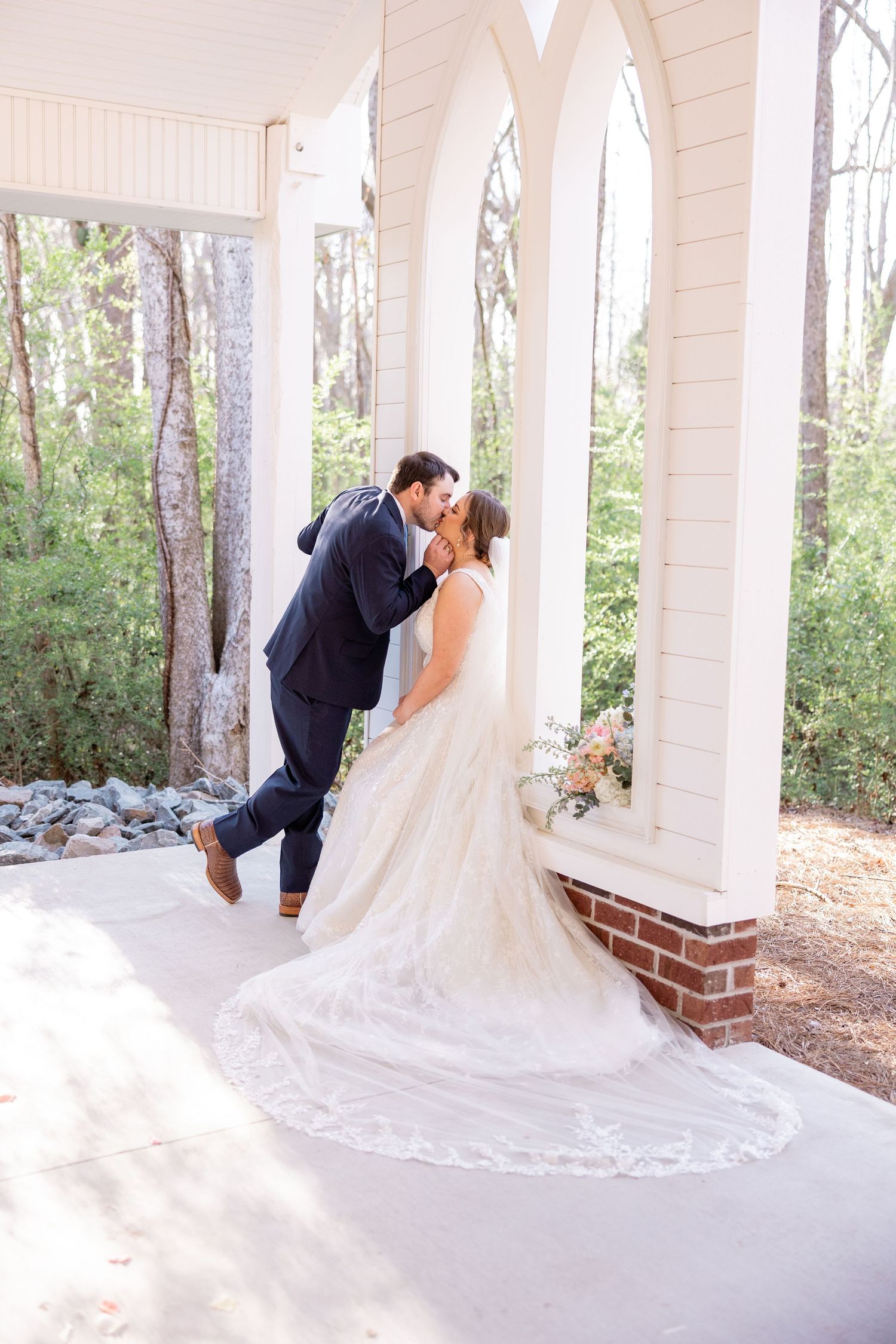 A romantic kiss between newlyweds on a covered porch with a flowing wedding dress train.