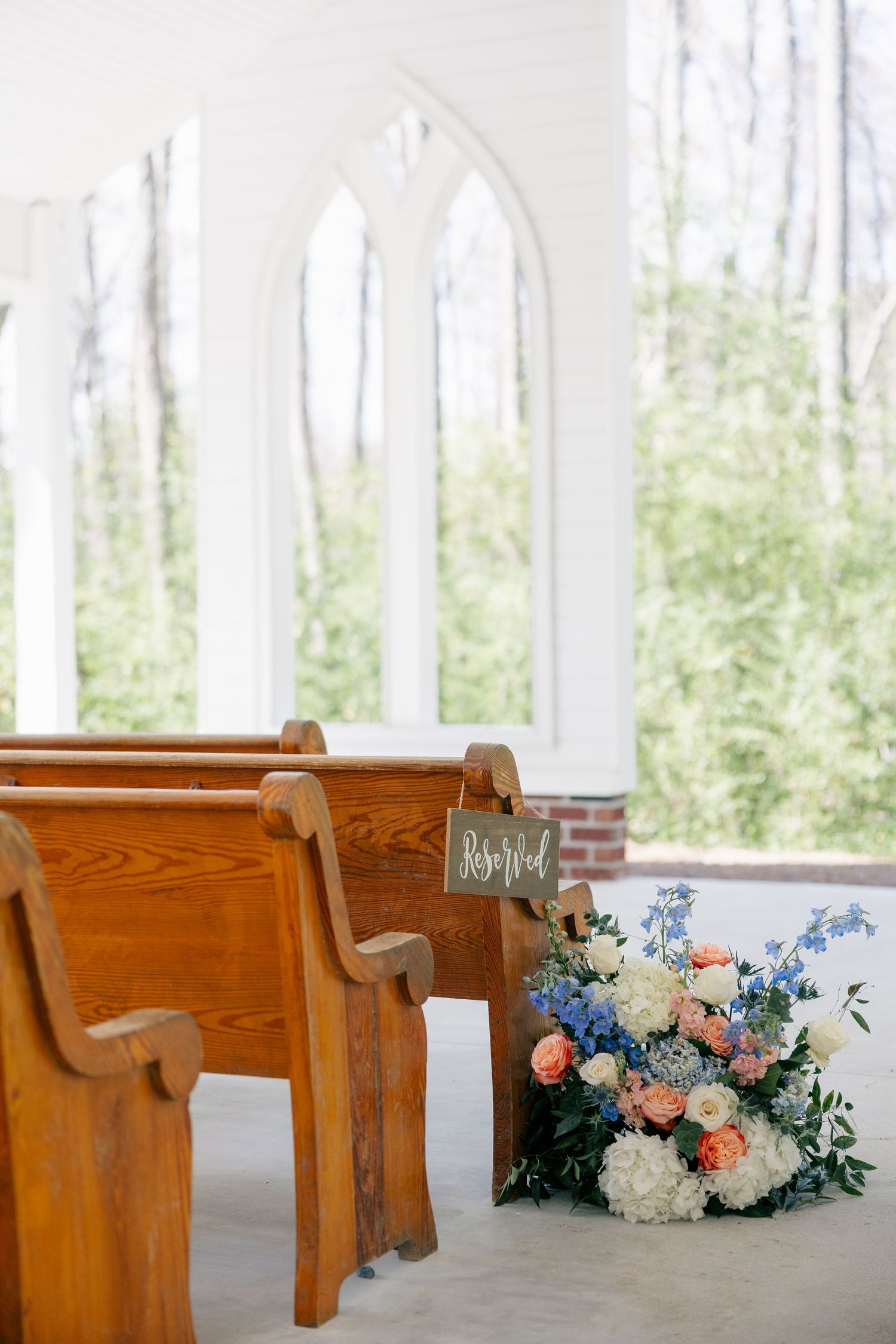 Wooden church pews decorated with delicate blue and peach floral arrangements in a bright chapel setting.