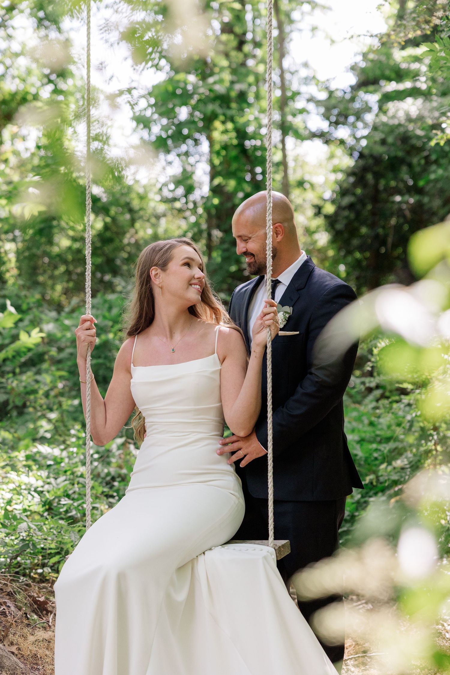 A couple shares a romantic moment on a swing set surrounded by lush greenery.
