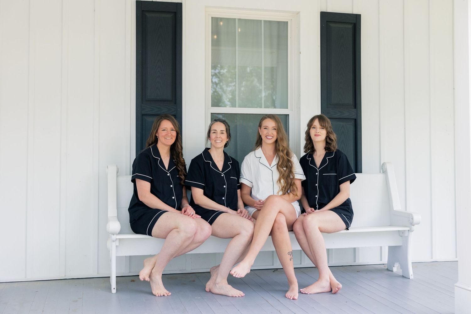 Group sitting on white porch with black shutters of country farmhouse.
