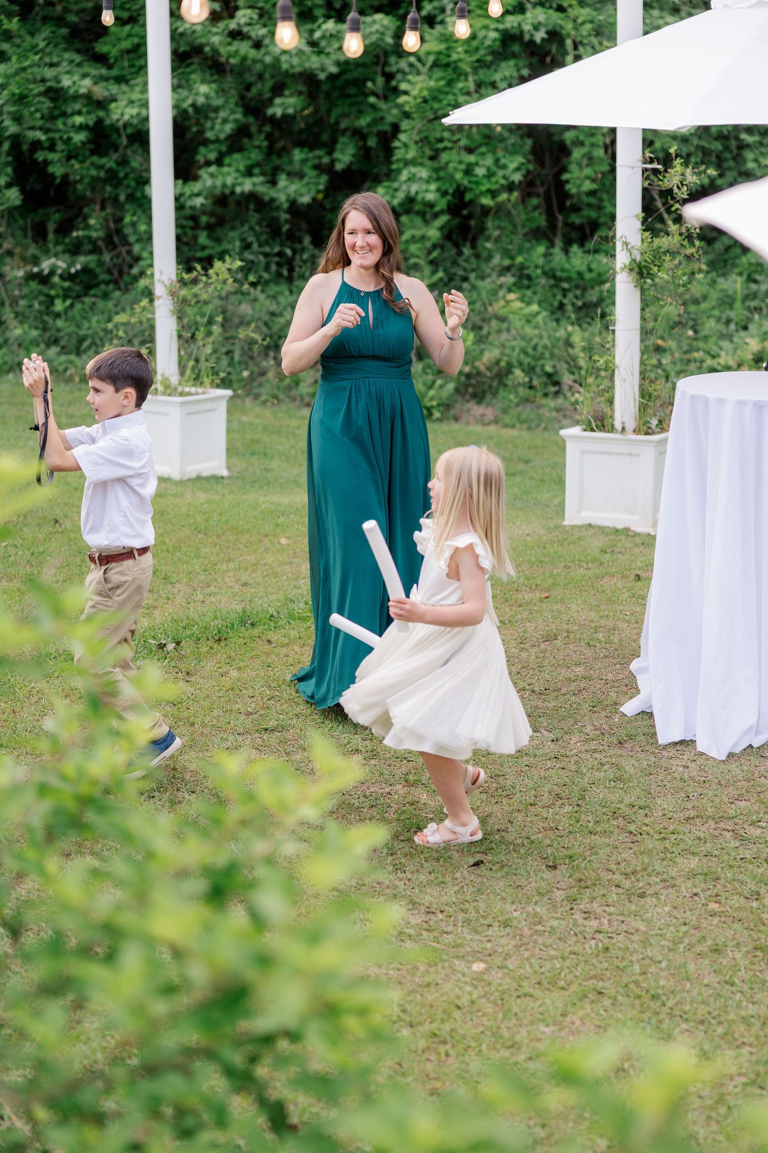 Children and guests in formal attire dance at an outdoor wedding reception under white tents.