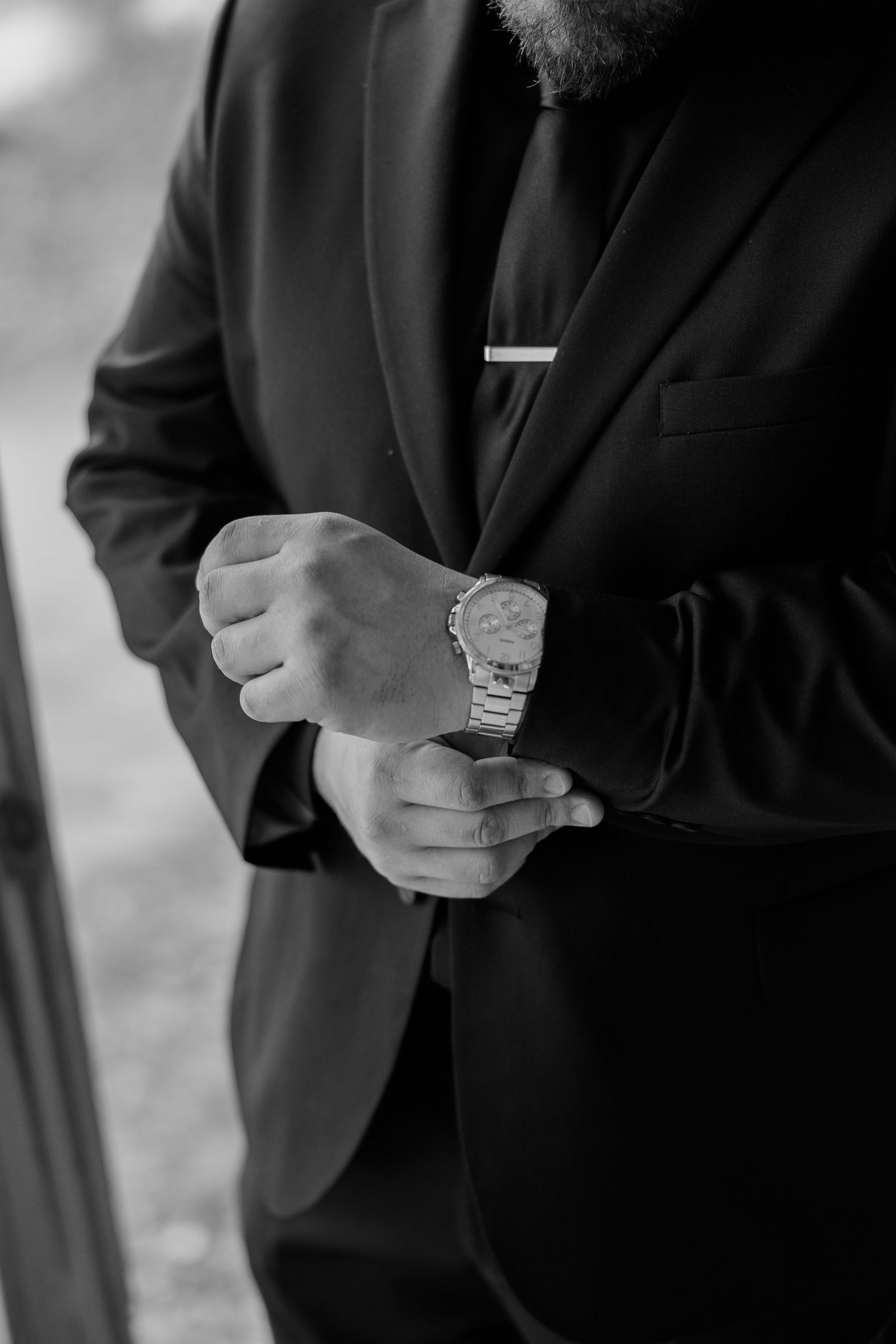 Close-up details of men in black suits adjusting their watches and cuffs.