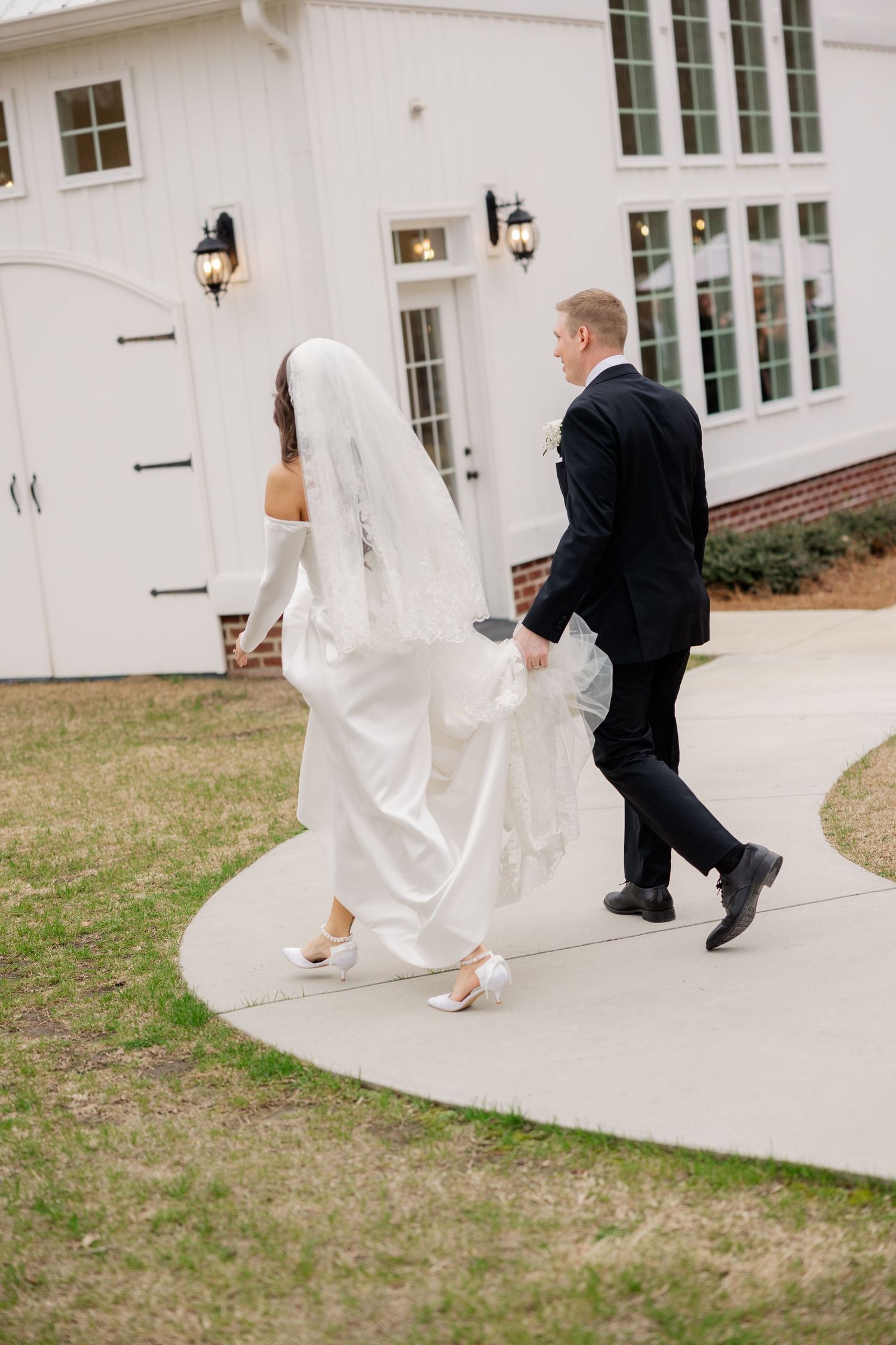 Wedding couple walking along a curved white building pathway in formal attire.