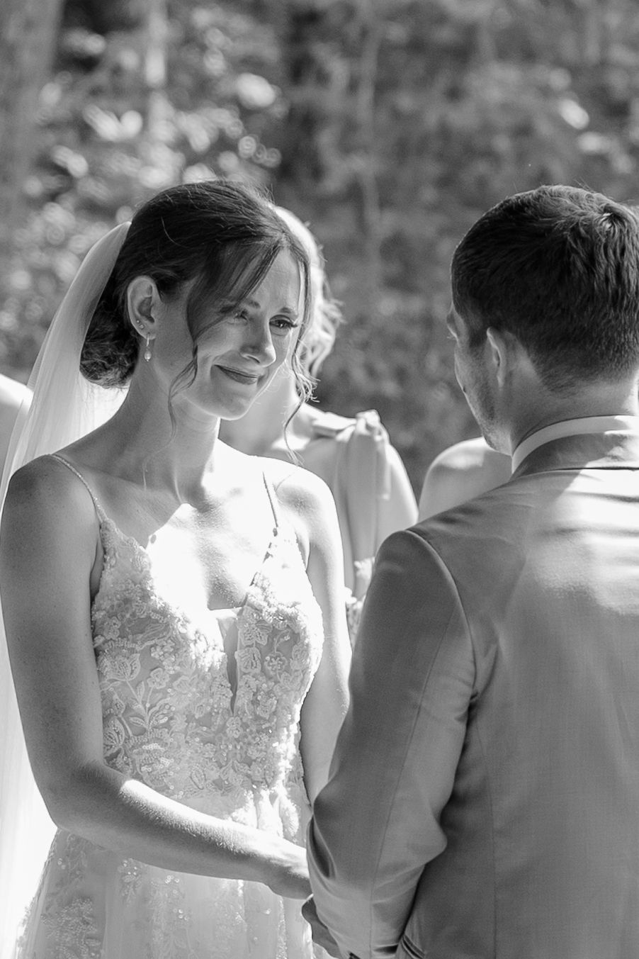 A tender moment at a wedding ceremony shows a couple in white dress and gray suit standing close together outdoors.