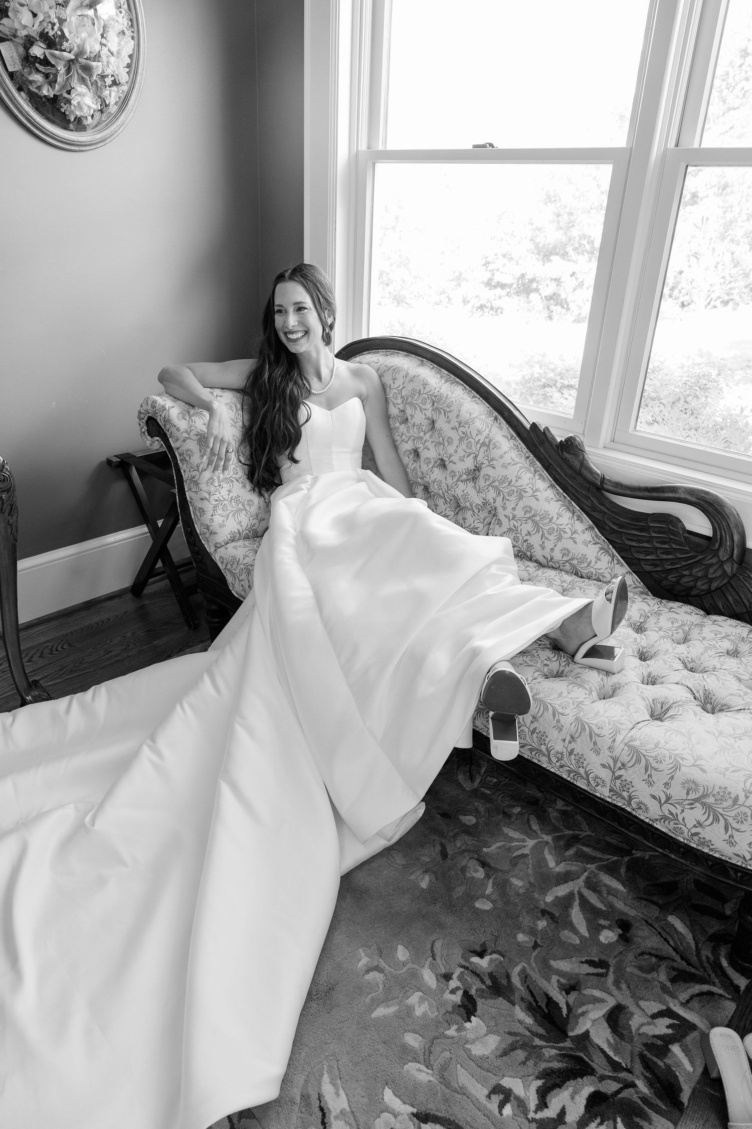 A white wedding dress elegantly draped across a vintage floral couch in a sunlit room.