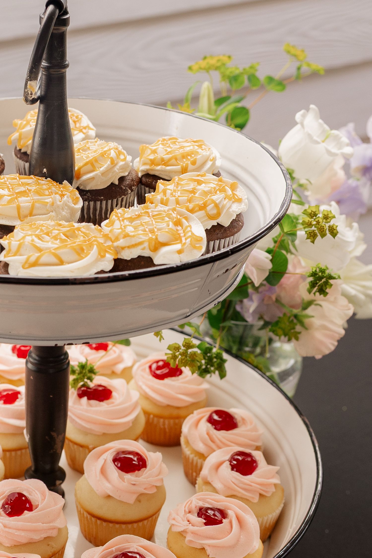 Pink frosted cupcakes with cherries on top arranged on black and white plates with floral decorations.