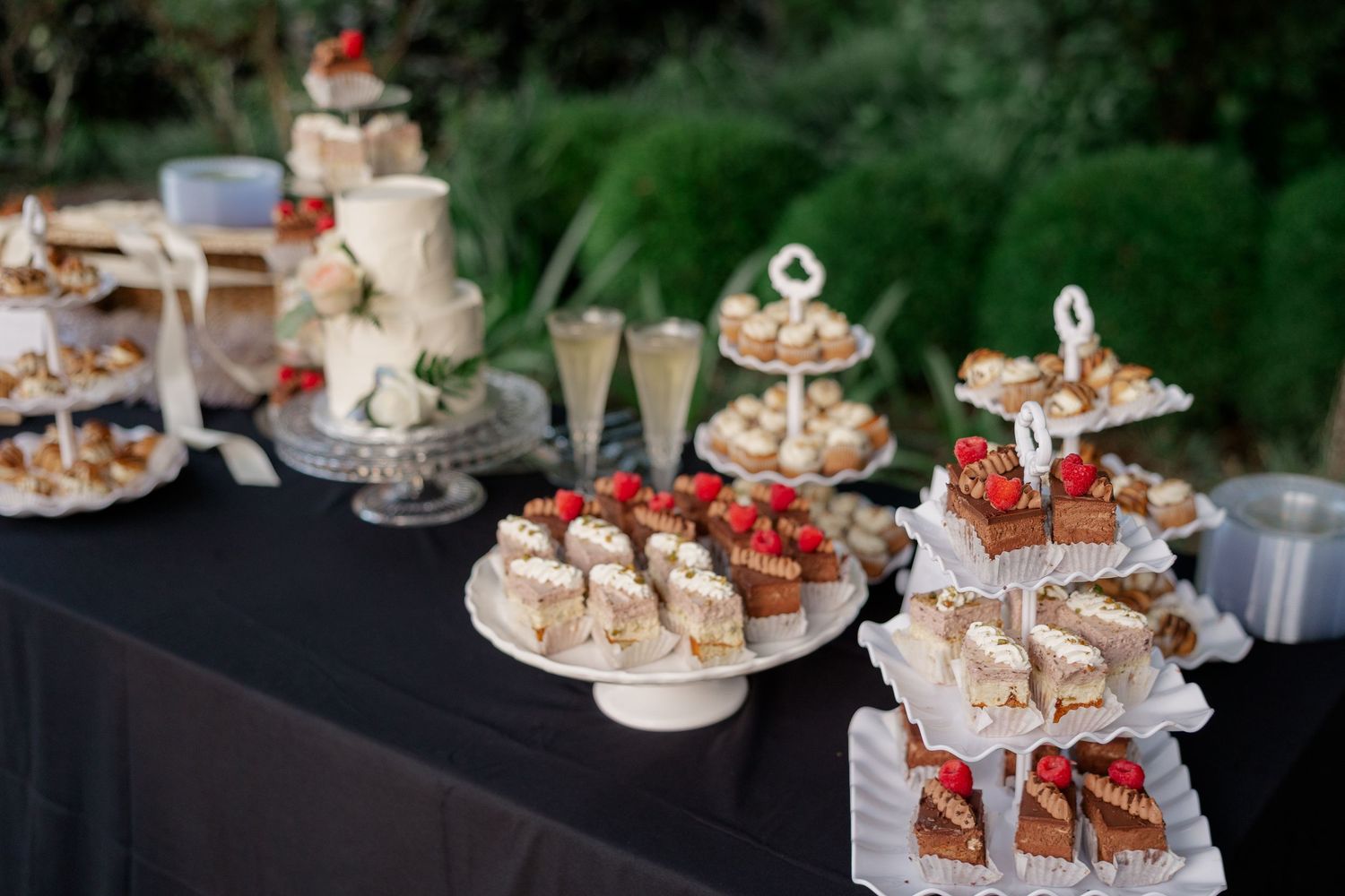 Elegant dessert display featuring tiered platters of cupcakes and pastries at an outdoor event.