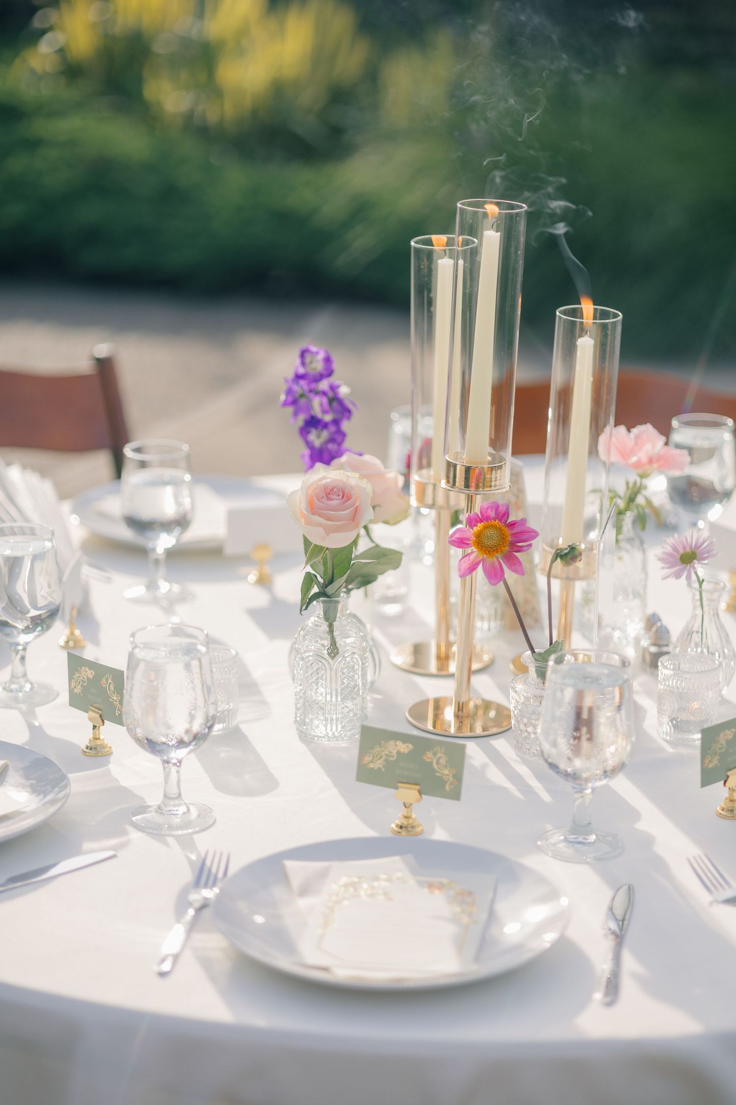 Elegant table setting with tall gold candleholders, delicate floral arrangements in crystal vases, and pristine white plates.