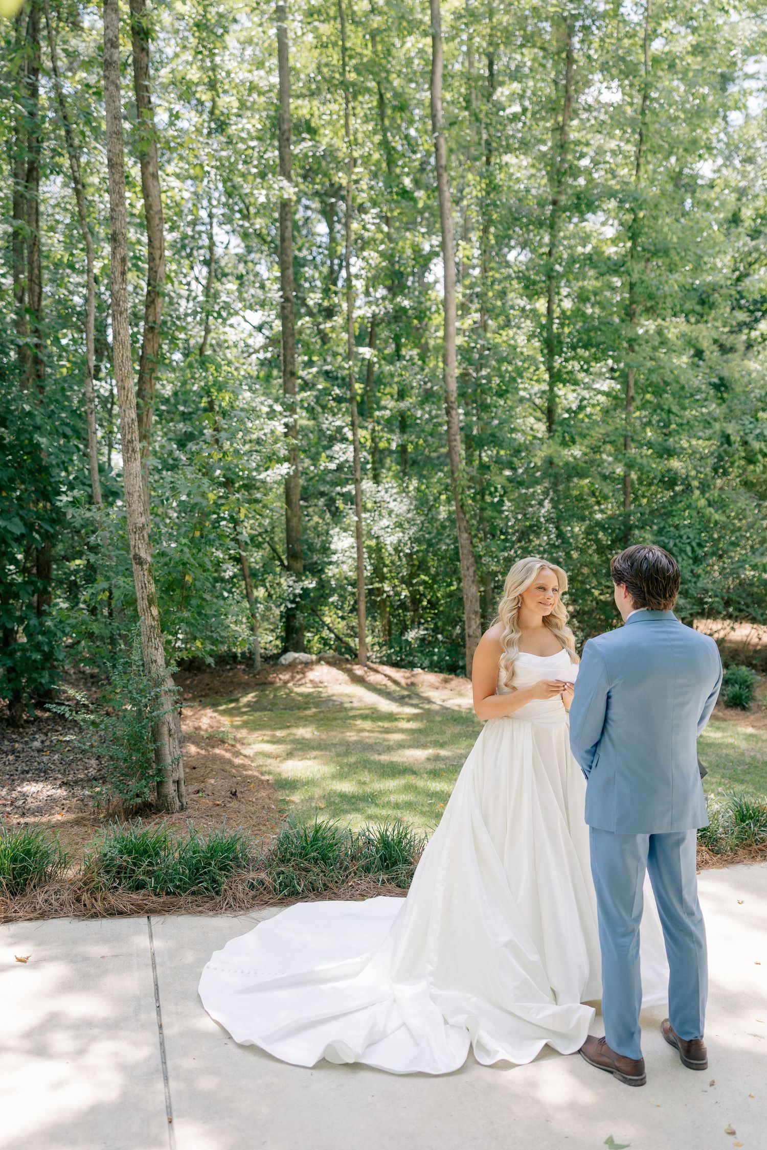 Bride in elegant gown with long train stands with groom in blue suit.
