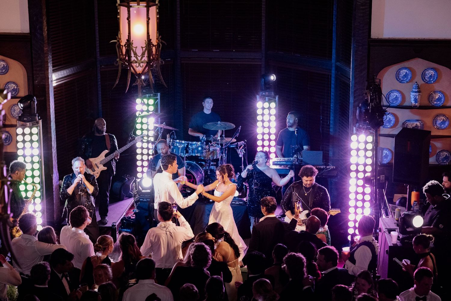 Bride and groom dance on stage with live band performing at vibrant wedding reception celebration.