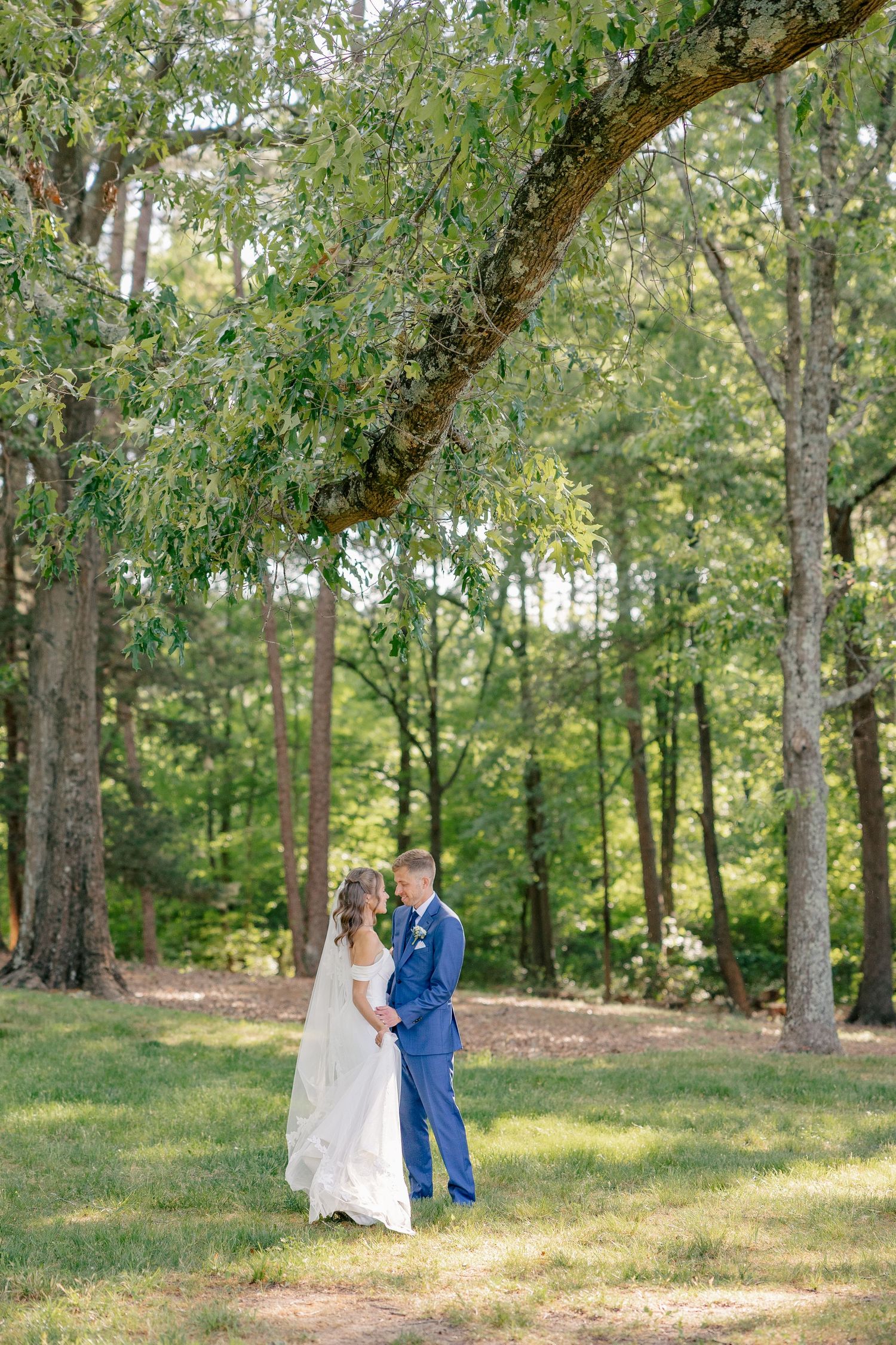 Bride and groom share intimate moment under large tree canopy in lush green forest setting.