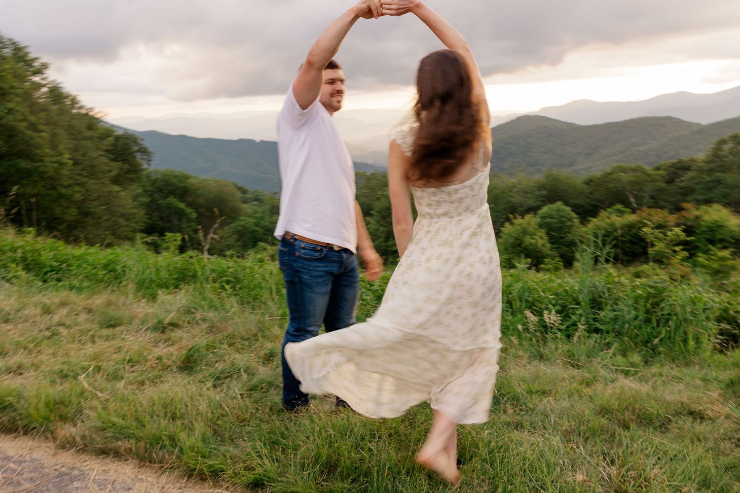 A couple dancing together on a mountain path with a scenic valley view behind them.