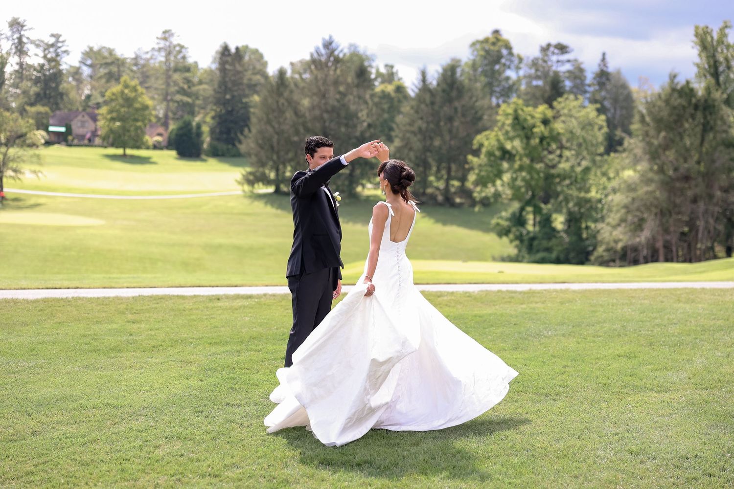 Bride and groom dance and twirl on lush green golf course lawn on sunny wedding day.