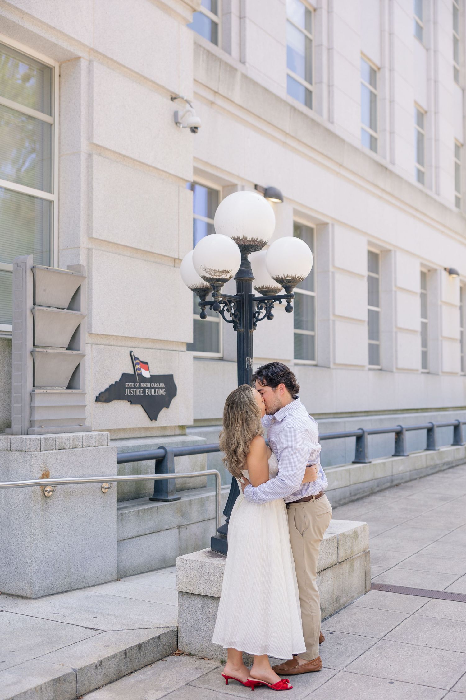 Couple sharing romantic kiss beside decorative lamp post outside historic judicial building.